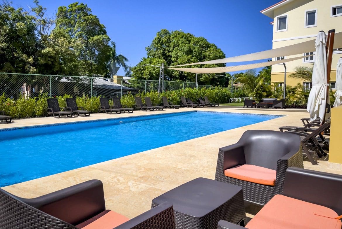 buyDRproperty Poolside lounge area with chairs, pool, and building, offering modern comfort. Sosua Real Estate