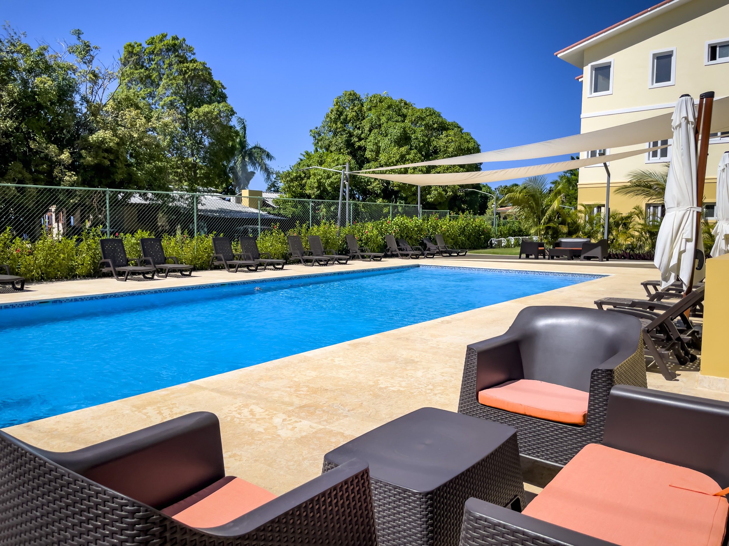 buyDRproperty Poolside lounge area with chairs, pool, and building, offering modern comfort. Sosua Real Estate