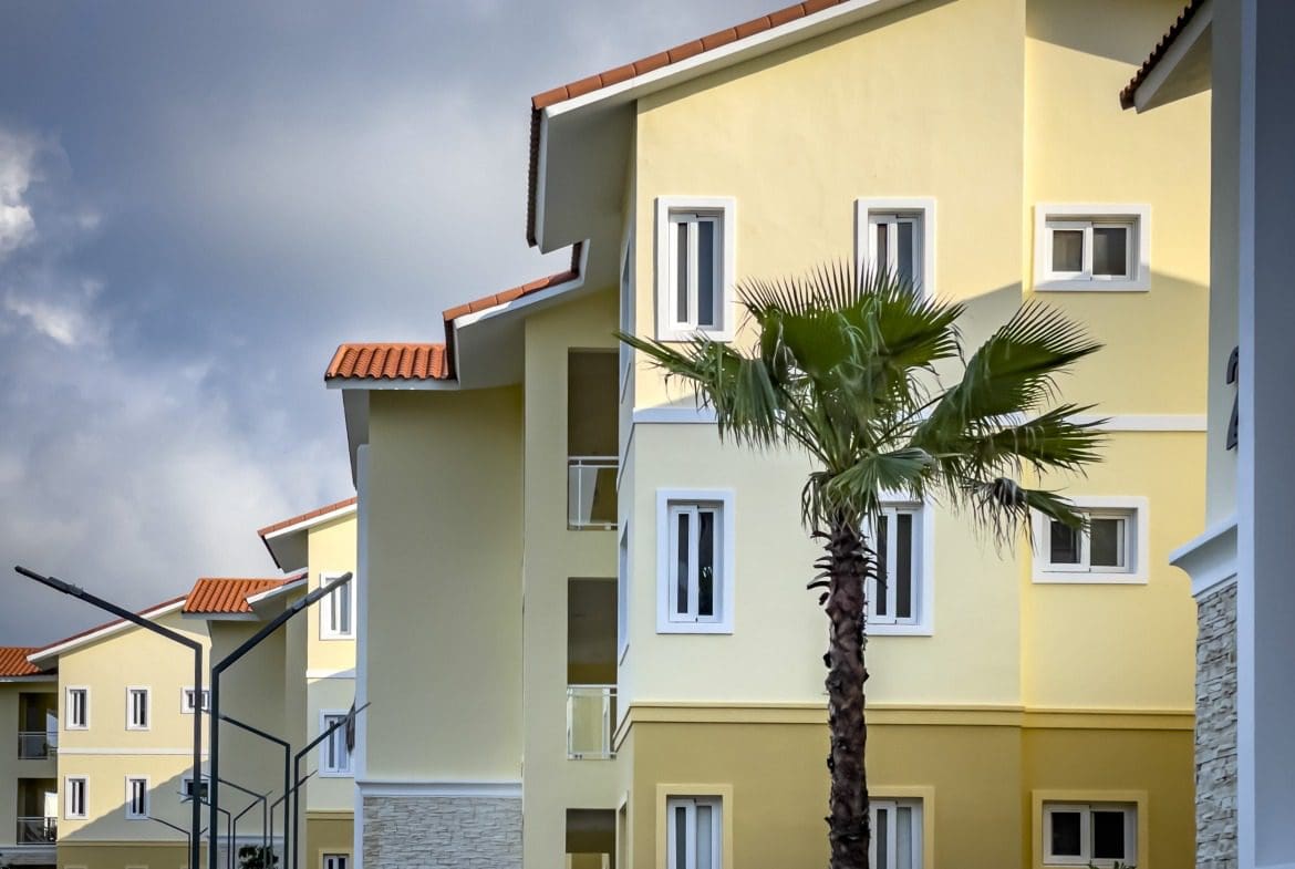 buyDRproperty Modern 1-bedroom condo building with palm tree and orange tile roof. Sosua Real Estate