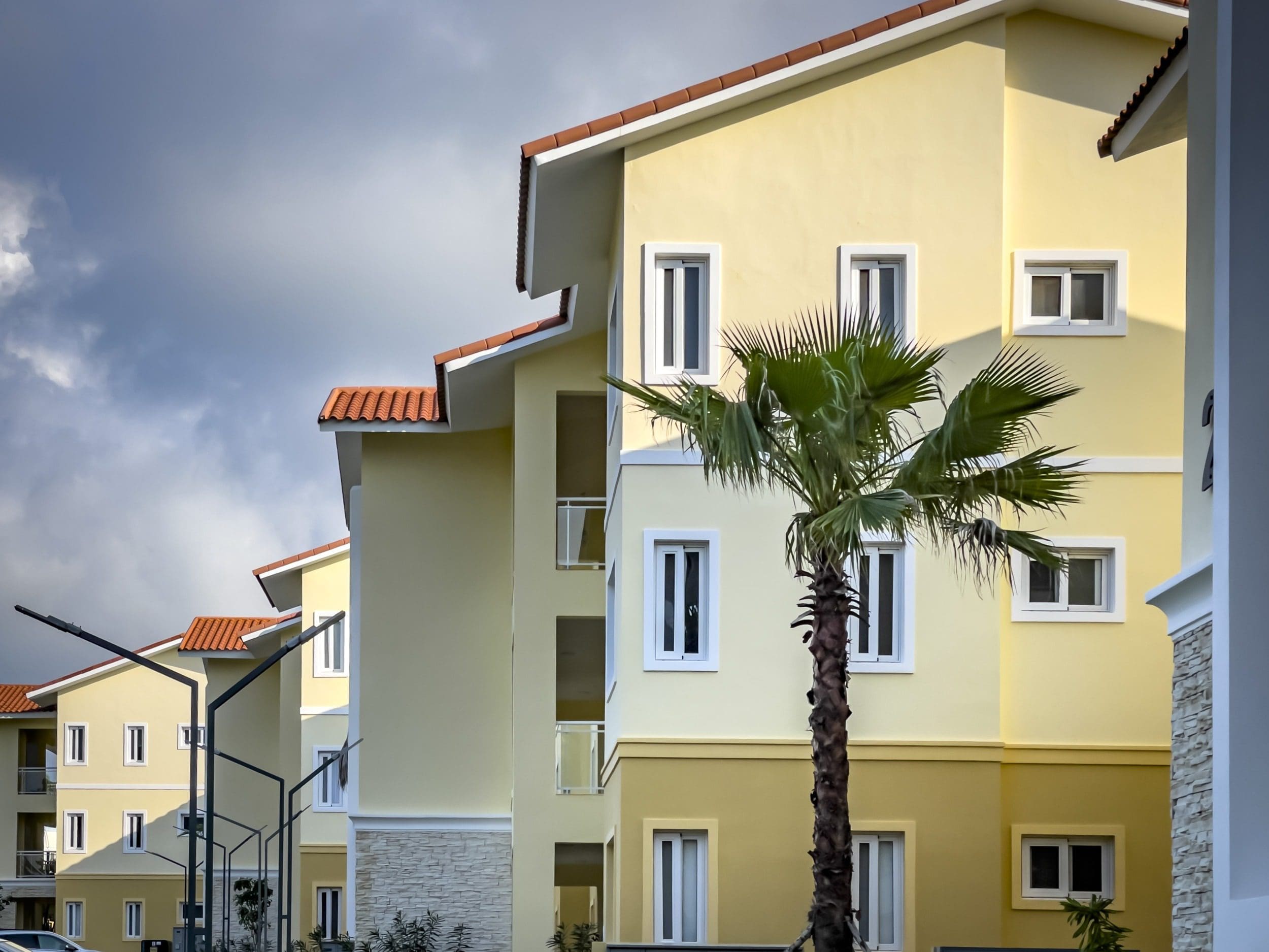 buyDRproperty Modern 1-bedroom condo building with palm tree and orange tile roof. Sosua Real Estate