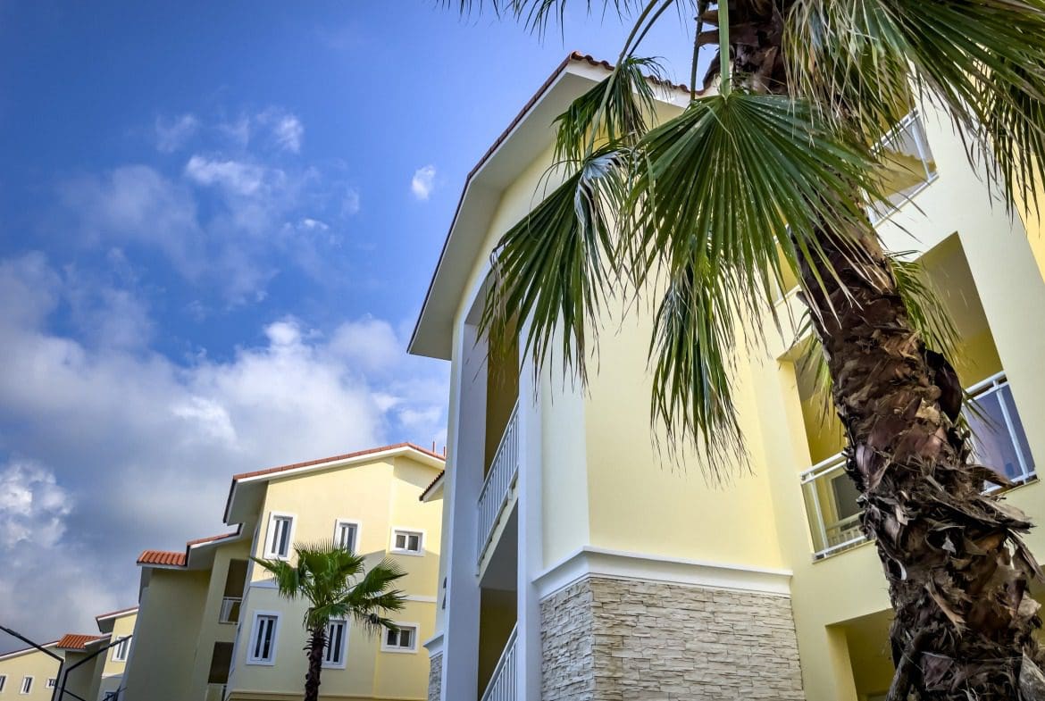 buyDRproperty Modern 1-bedroom condo exterior with palm trees and blue sky Sosua Real Estate