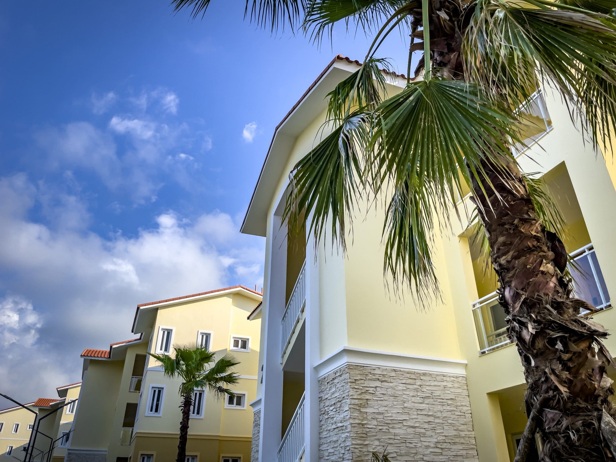 buyDRproperty Modern 1-bedroom condo exterior with palm trees and blue sky Sosua Real Estate