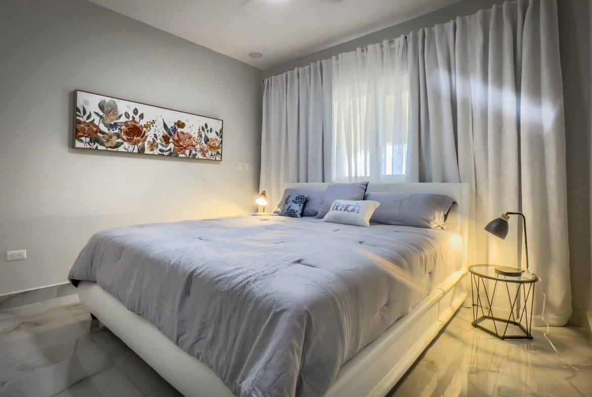 buyDRproperty Cozy 1-bedroom condo bedroom with a comfortable bed and floral artwork. Sosua Real Estate