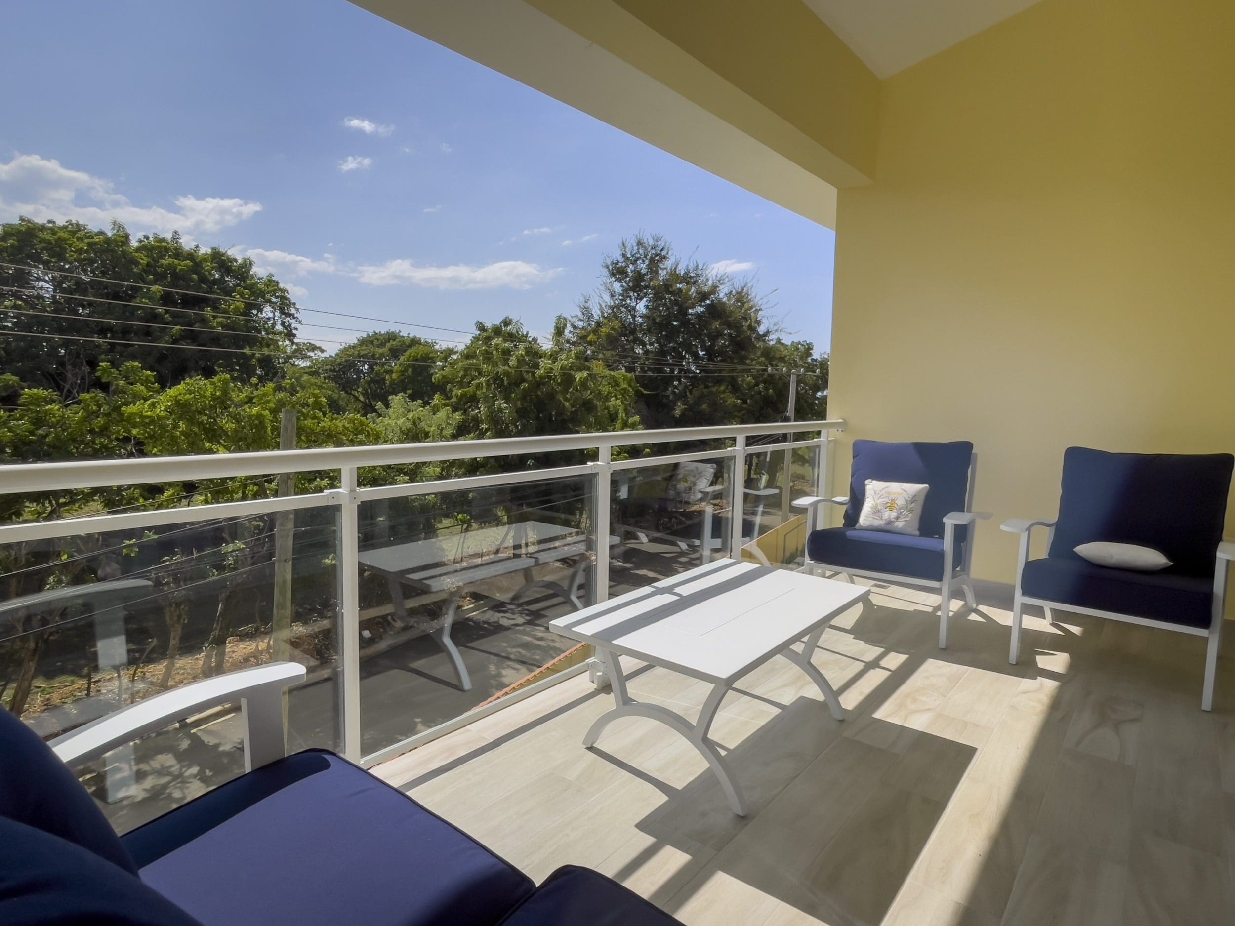 buyDRproperty Balcony of a 1-Bedroom Condo with blue chairs, white table, and glass railing. Sosua Real Estate