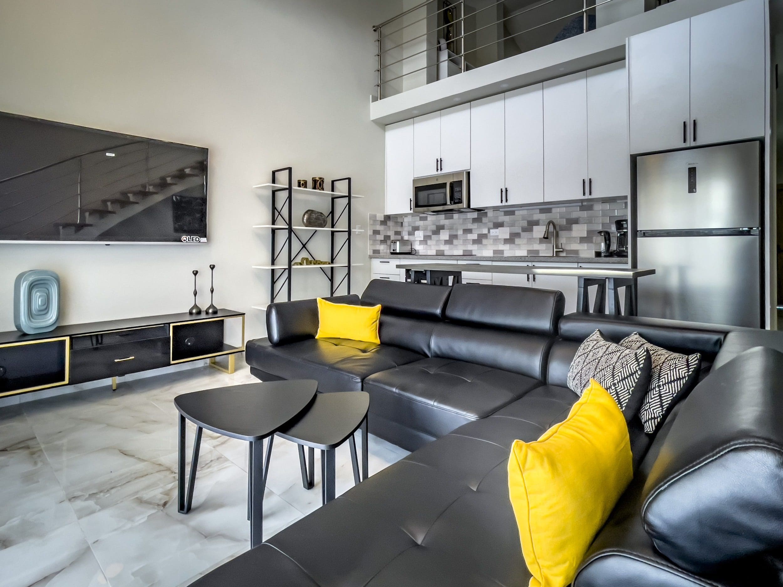 buyDRproperty Modern 1-bedroom condo living room with black leather sectional sofa and kitchen in the background. Sosua Real Estate