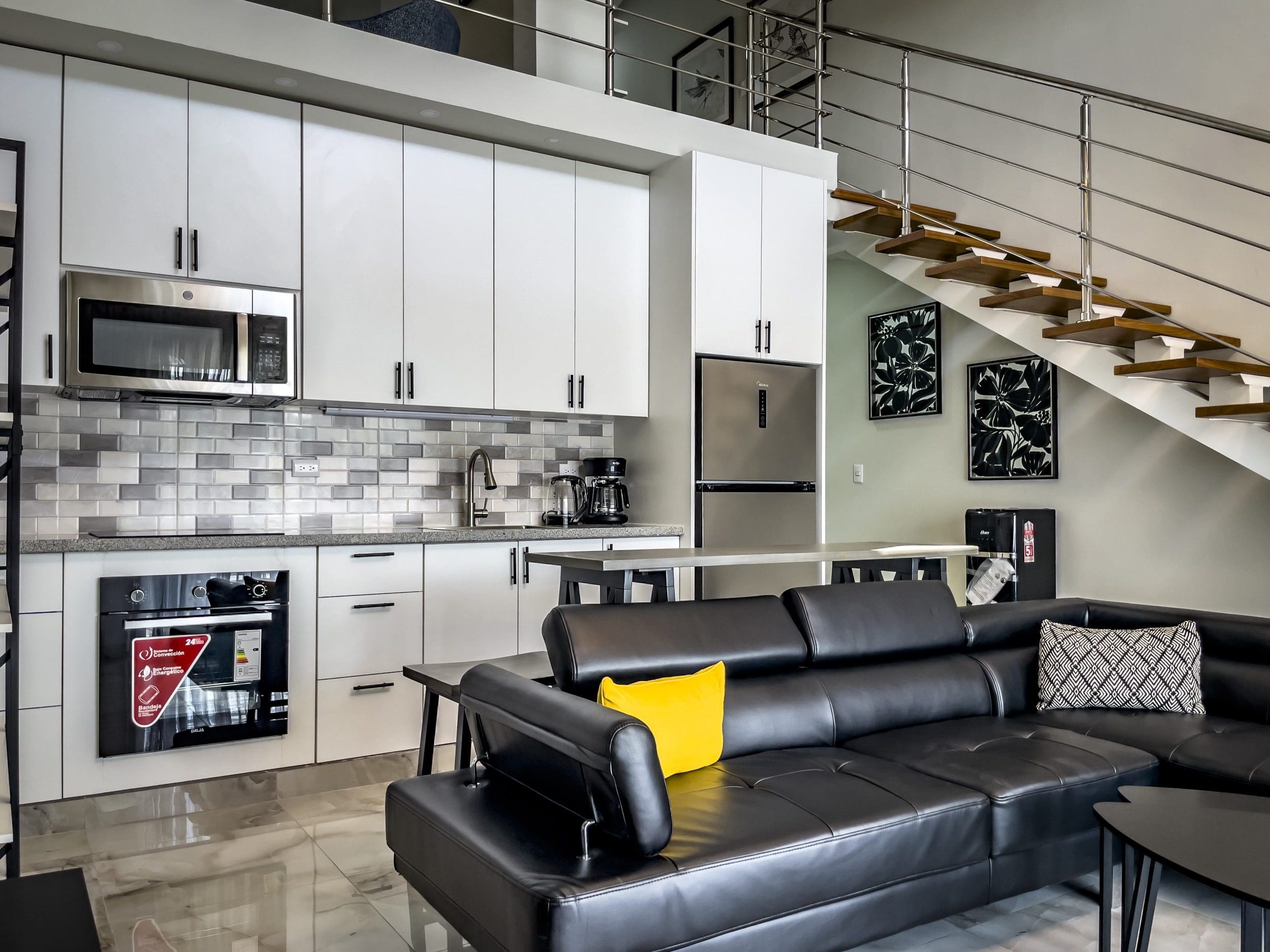 buyDRproperty Modern 1-Bedroom Condo kitchen with white cabinets, stainless steel appliances, and black leather sofa. Sosua Real Estate