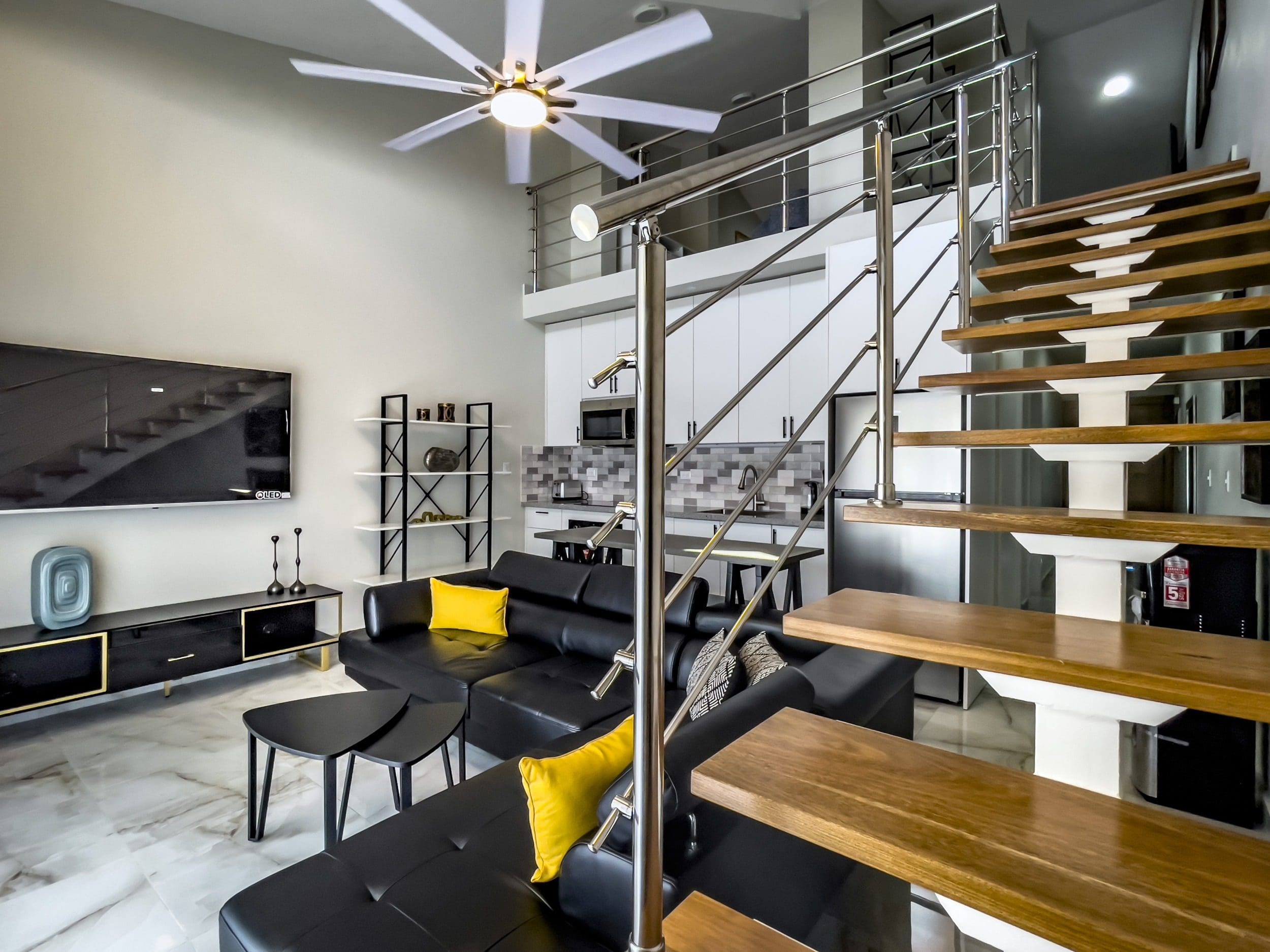 buyDRproperty Stylish 1-Bedroom Condo living room with black leather sofa, loft stairs and modern kitchen. Sosua Real Estate