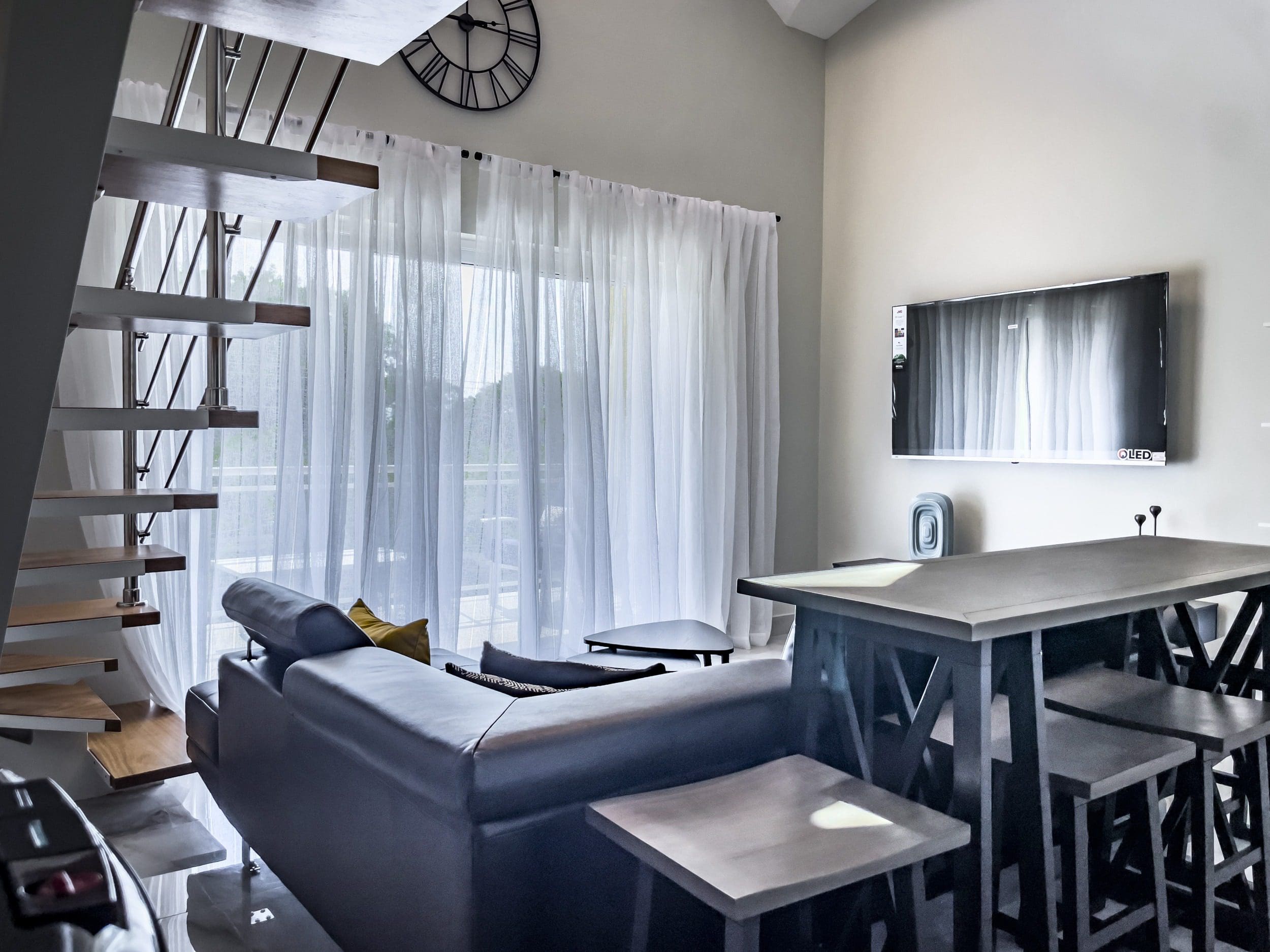buyDRproperty Modern 1-bedroom condo living room with floating staircase, sofa, and TV. Sosua Real Estate