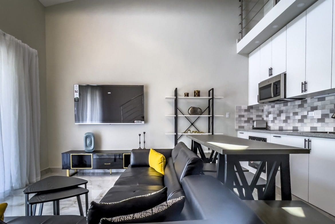 buyDRproperty Stylish 1-Bedroom Condo living room with black leather sofa and modern kitchen. Sosua Real Estate