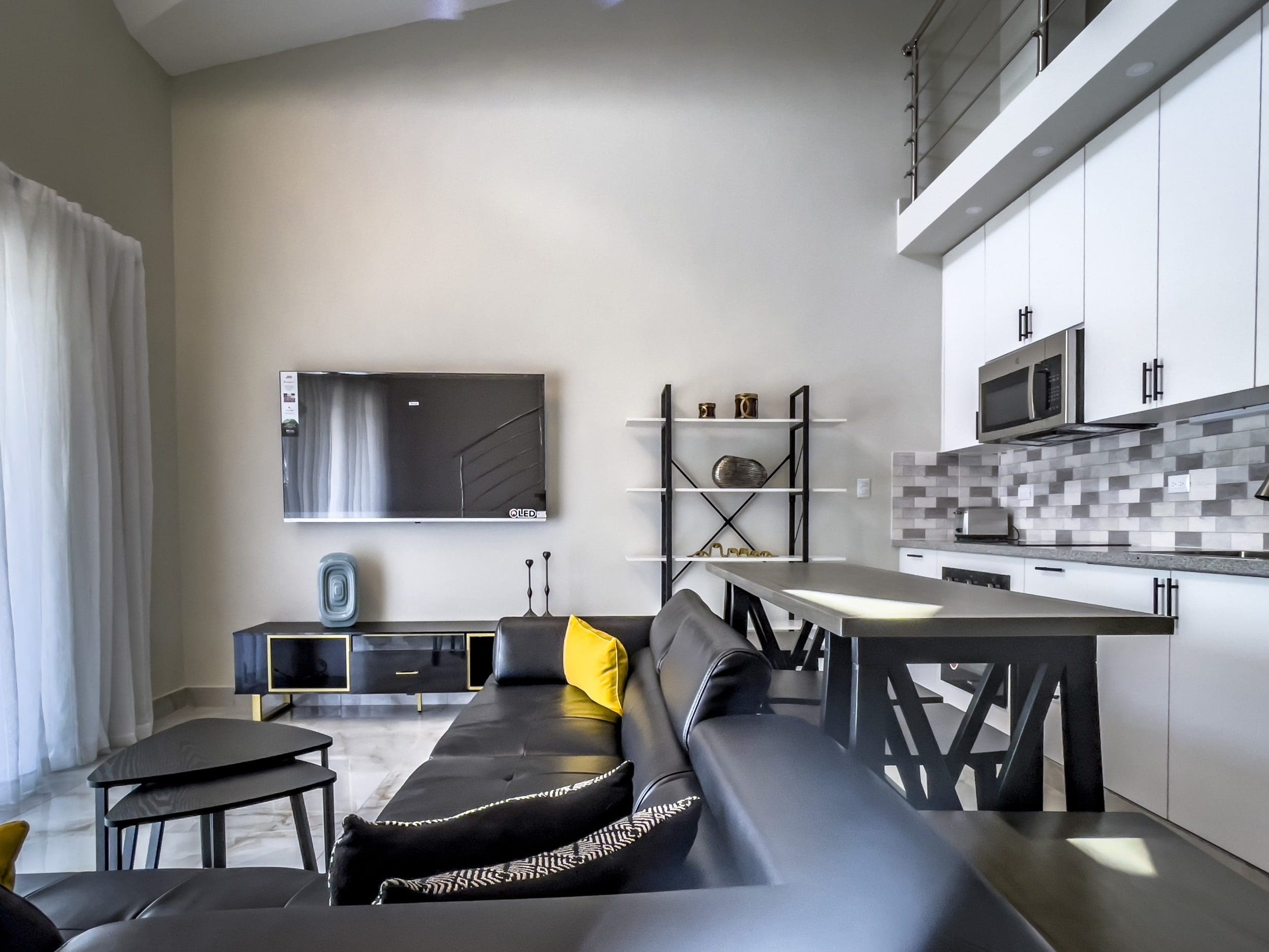 buyDRproperty Stylish 1-Bedroom Condo living room with black leather sofa and modern kitchen. Sosua Real Estate