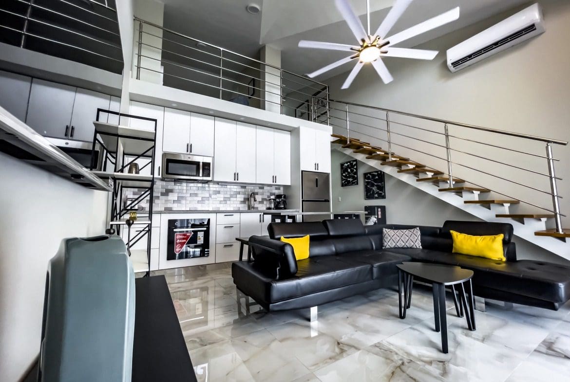 buyDRproperty Modern 1-bedroom condo interior with black leather sofa and staircase. Sosua Real Estate