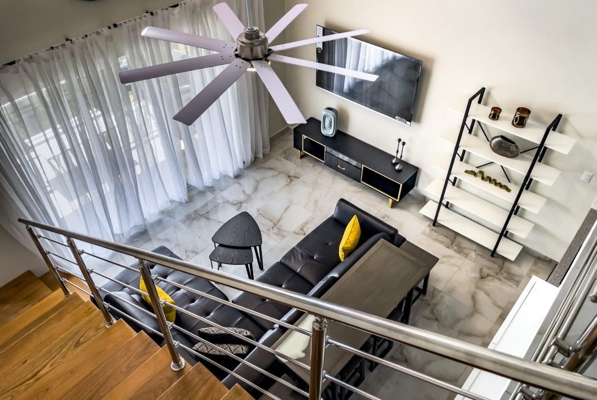 buyDRproperty Modern 1-Bedroom Condo living room with black leather sofa, ceiling fan, and marble floors. Sosua Real Estate