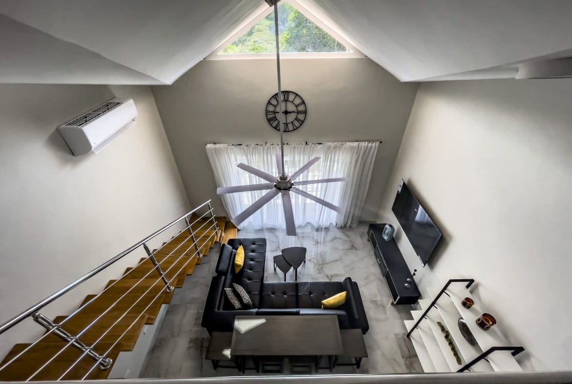 buyDRproperty Modern 1-Bedroom Condo interior with high ceiling, black sofa, and ceiling fan. Sosua Real Estate