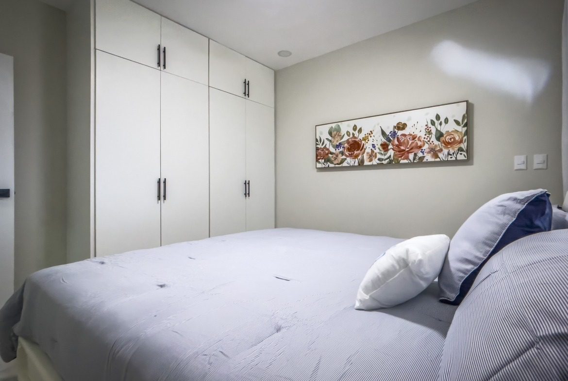 buyDRproperty Bedroom in a 1-bedroom condo with white cabinets and floral artwork. Sosua Real Estate