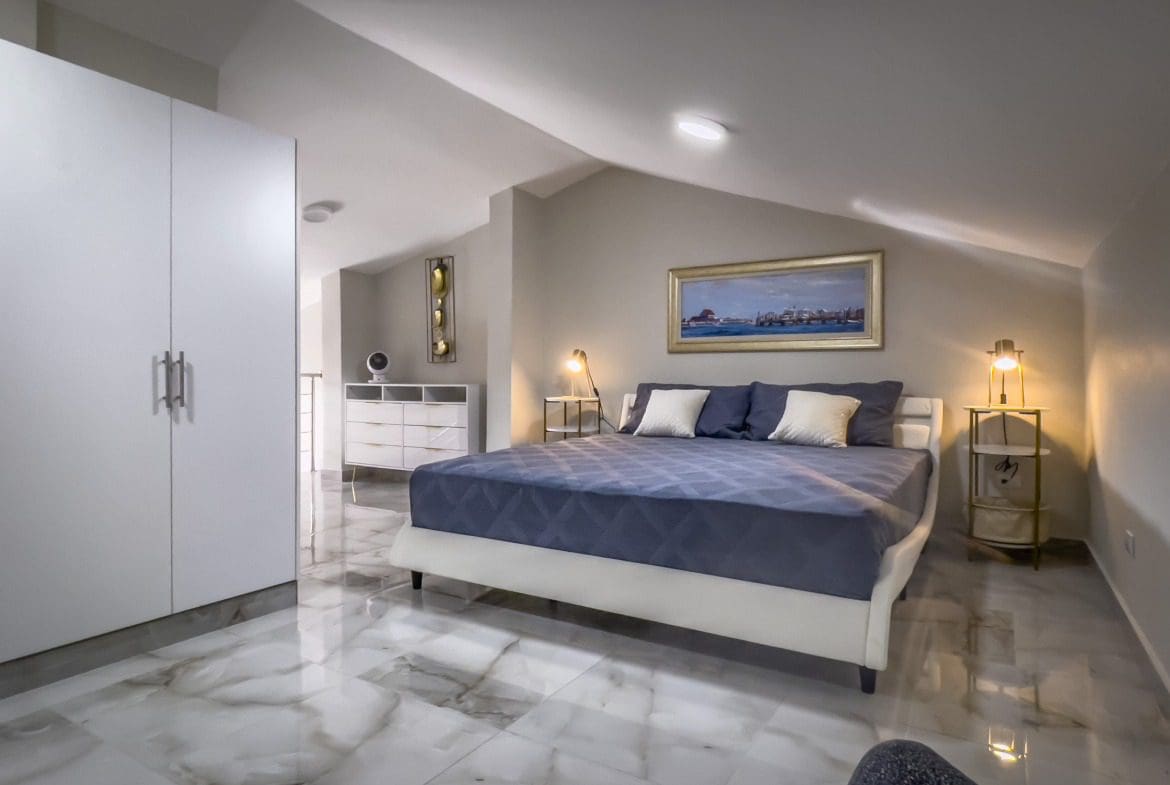 buyDRproperty Stylish loft bedroom in a 1-bedroom condo. Features a bed with blue comforter, bedside table, and art. Sosua Real Estate