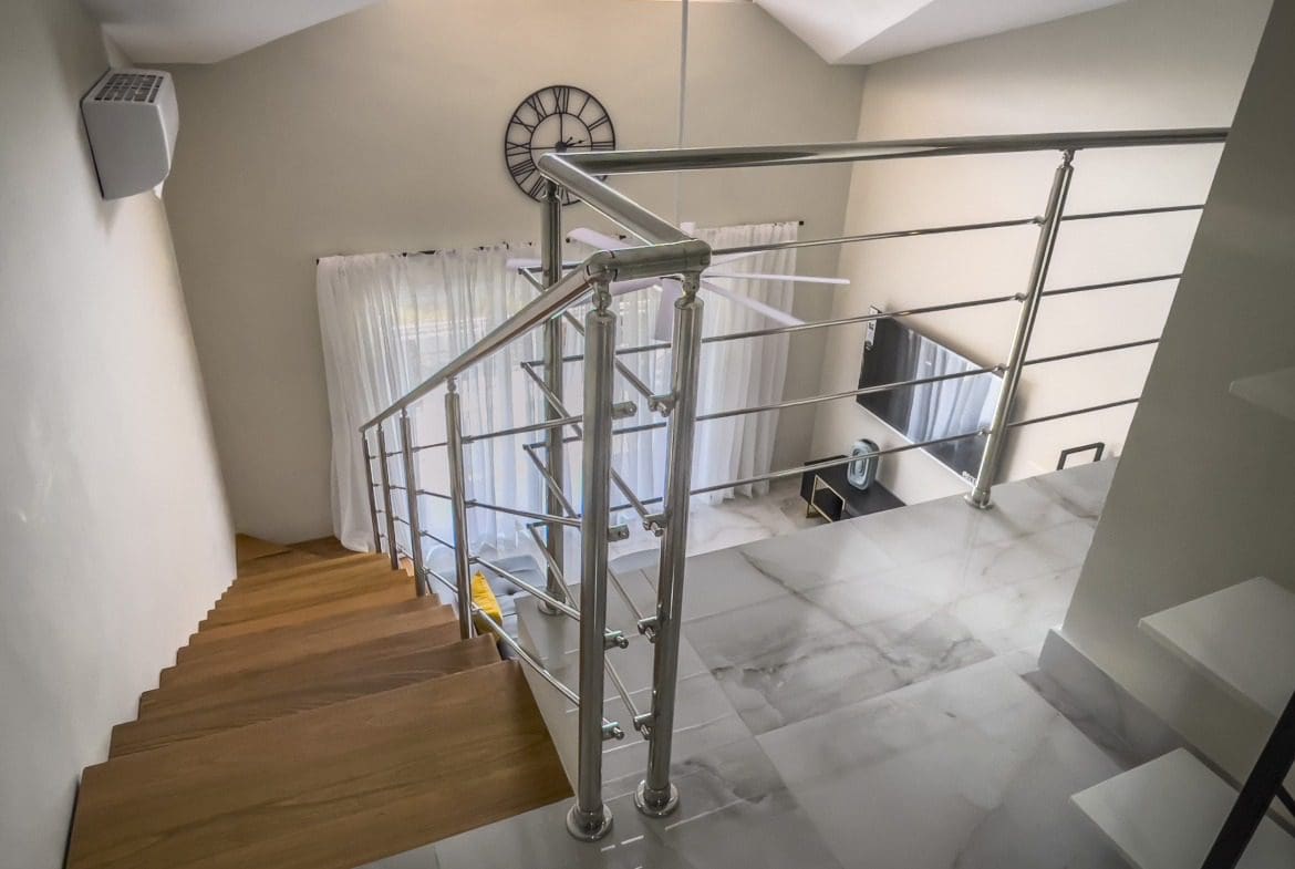 buyDRproperty Staircase in a modern 1-bedroom condo with stainless steel railing and wood steps. Sosua Real Estate