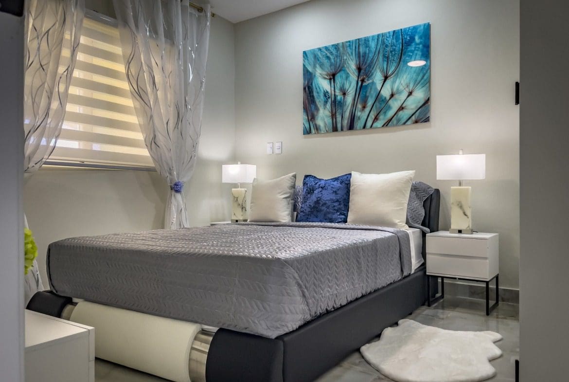 buyDRproperty Modern 1-Bedroom Condo bedroom with gray bedding, blue art, and white nightstands. Sosua Real Estate