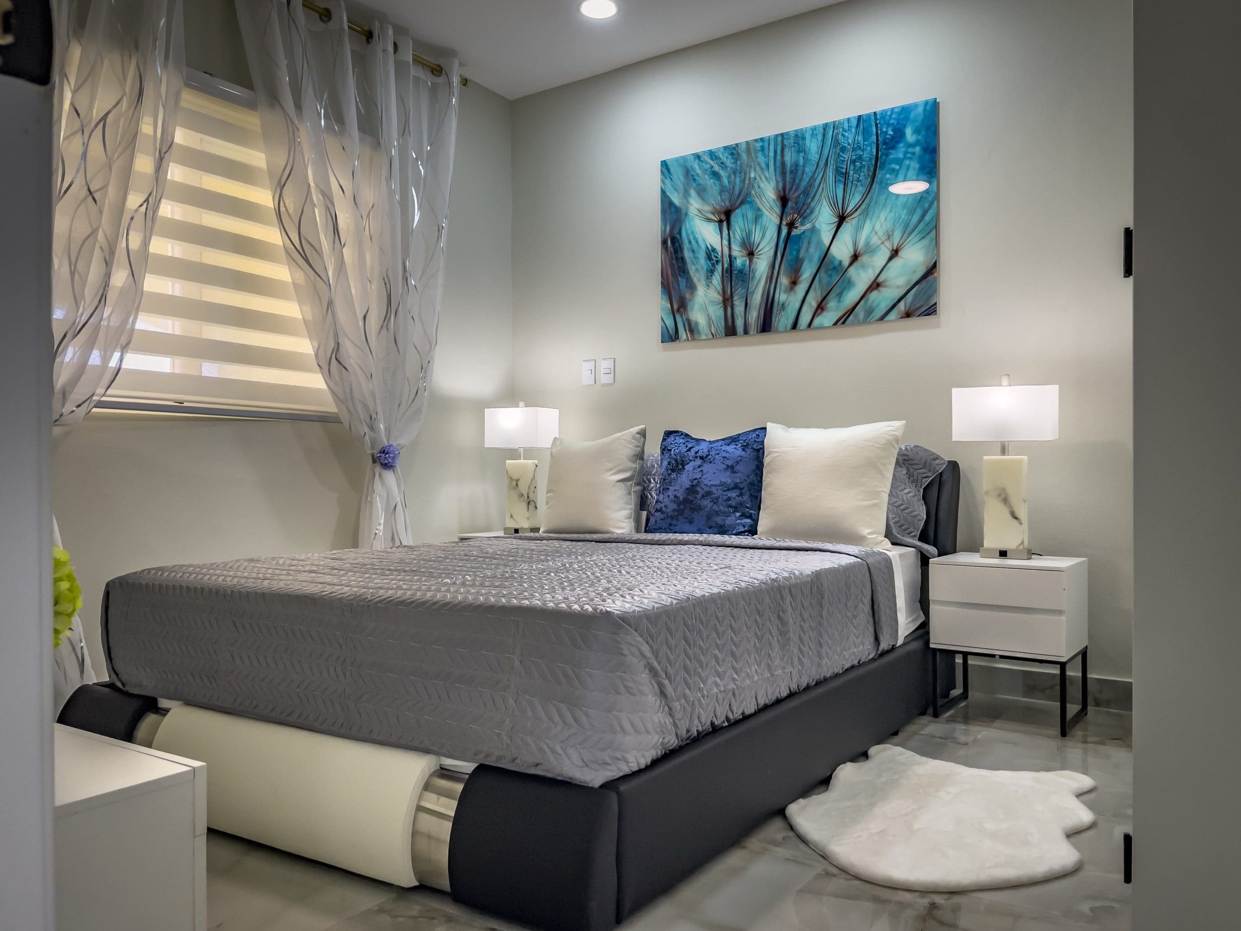 buyDRproperty Modern 1-Bedroom Condo bedroom with gray bedding, blue art, and white nightstands. Sosua Real Estate