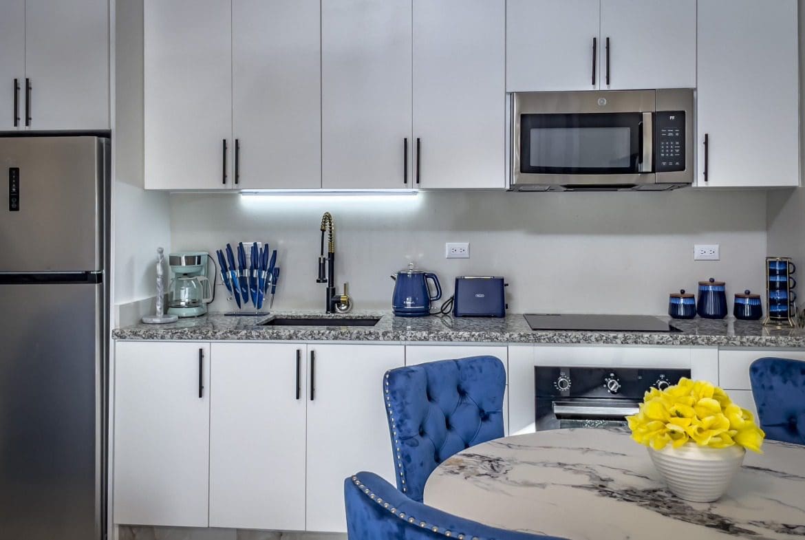 buyDRproperty Modern 1-bedroom condo kitchen with white cabinets, stainless steel appliances, and blue accents. Sosua Real Estate