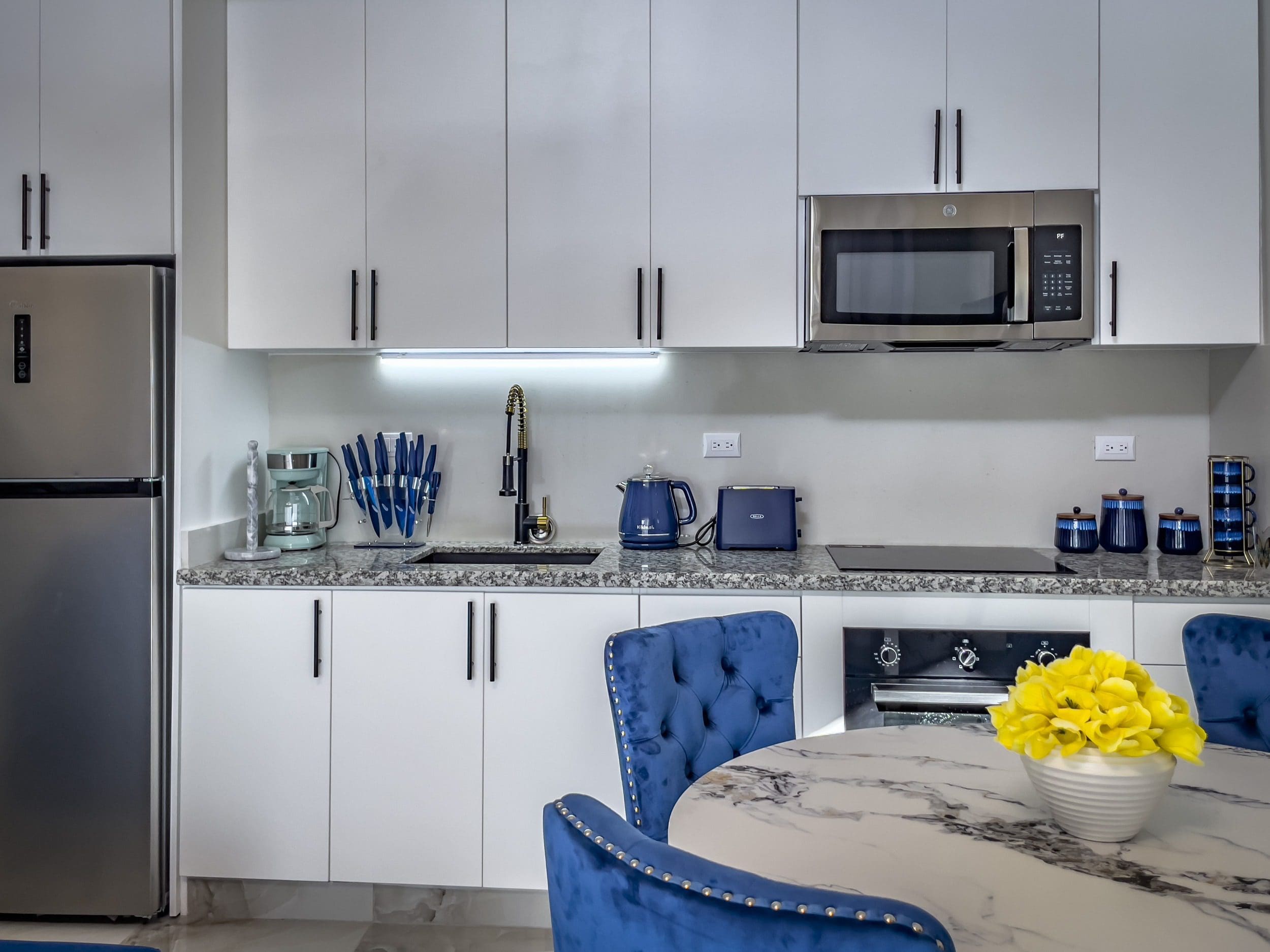 buyDRproperty Modern 1-bedroom condo kitchen with white cabinets, stainless steel appliances, and blue accents. Sosua Real Estate