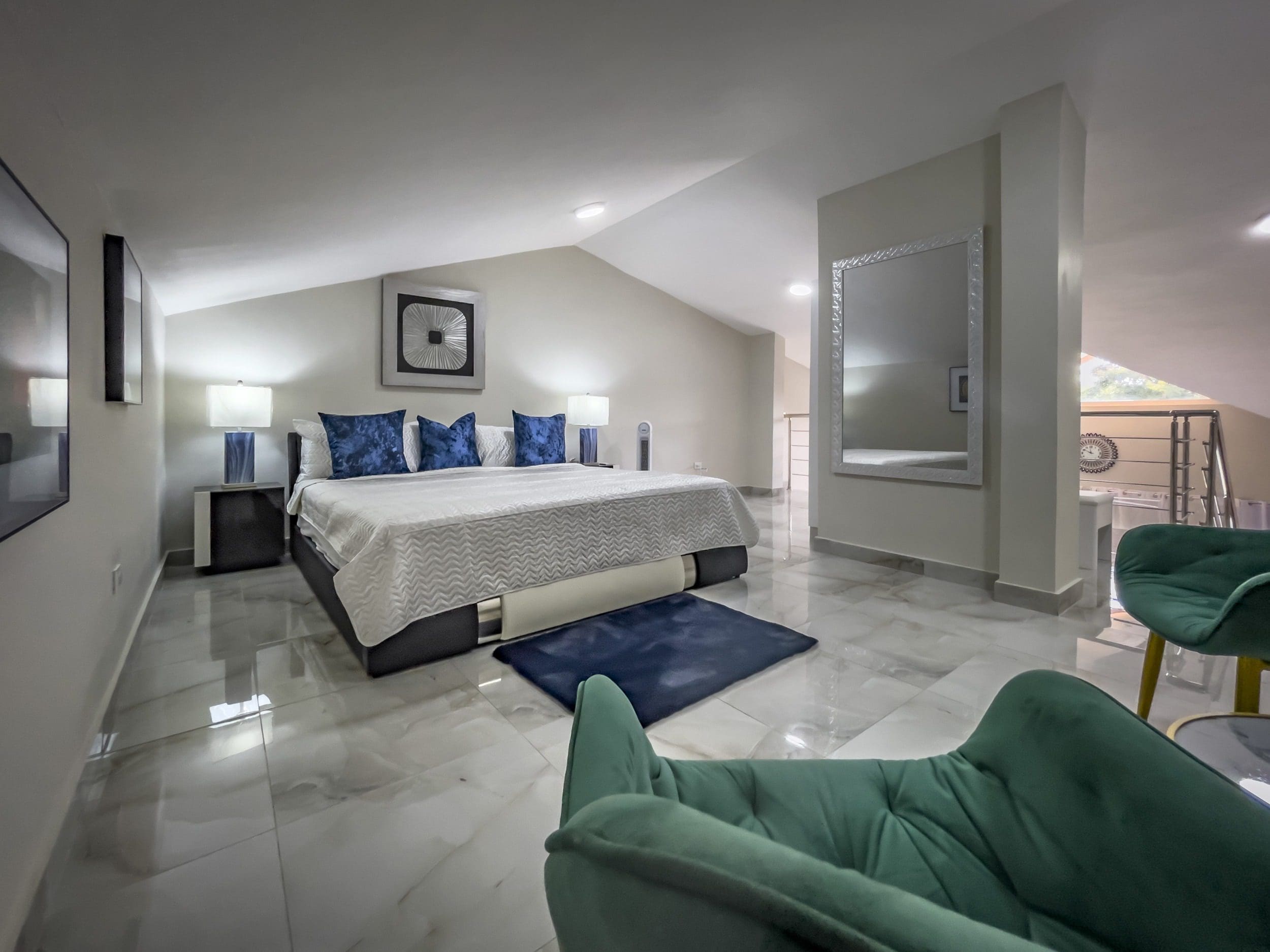 buyDRproperty Modern 1-bedroom condo bedroom with king bed, blue accents, and green chairs. Sosua Real Estate