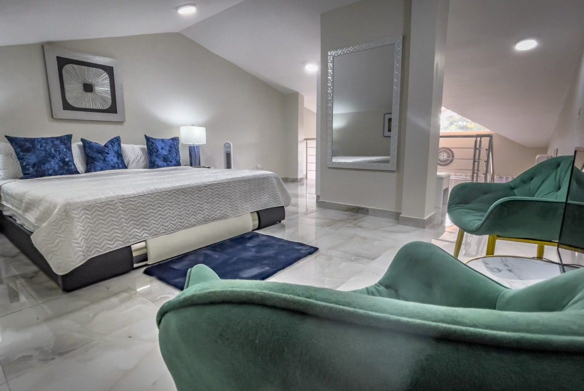 buyDRproperty Modern 1-bedroom condo bedroom with teal accent chairs, large mirror, and stylish decor. Sosua Real Estate
