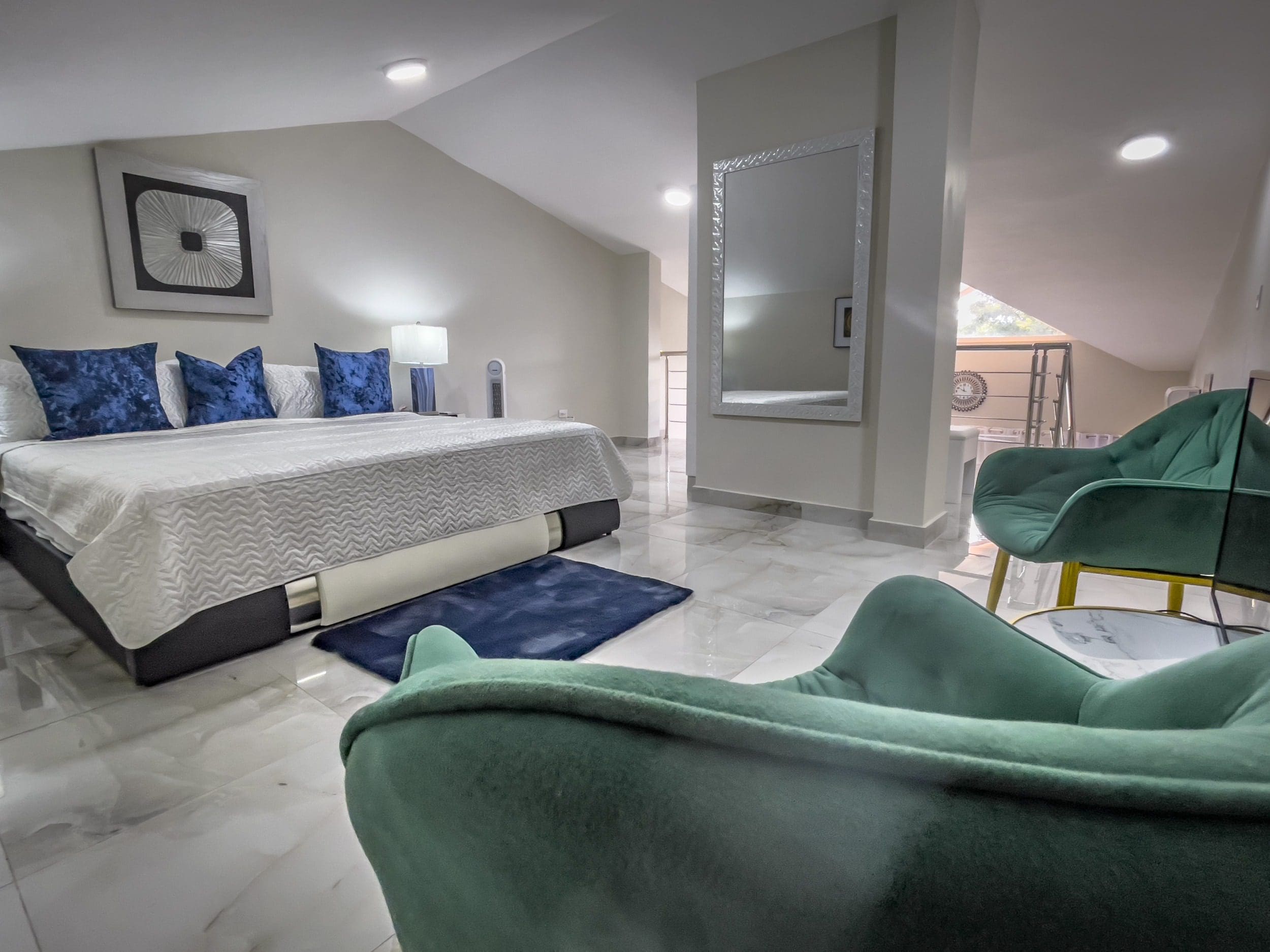 buyDRproperty Modern 1-bedroom condo bedroom with teal accent chairs, large mirror, and stylish decor. Sosua Real Estate