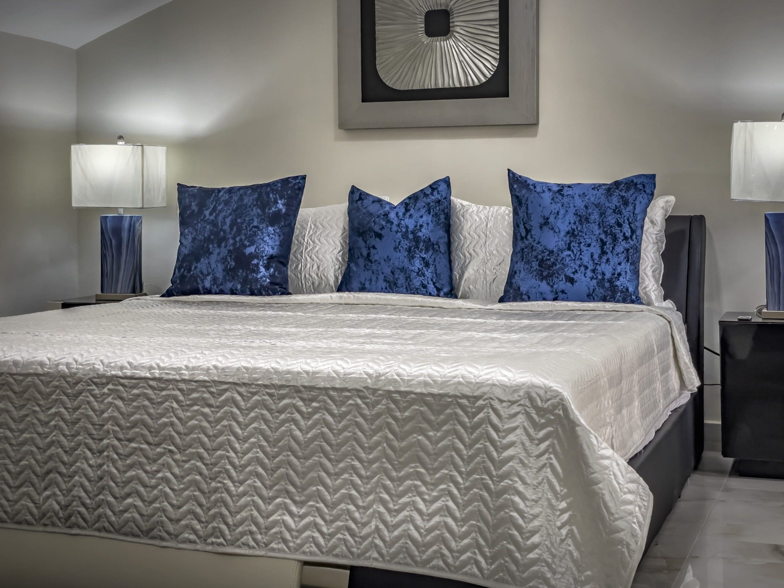 buyDRproperty Modern bedroom with blue velvet pillows and white bedding in a modern 1-bedroom condo. Sosua Real Estate