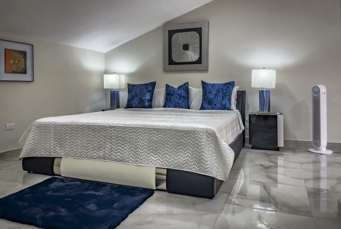 buyDRproperty Modern 1-bedroom condo bedroom with blue pillows and a white bedspread. Sosua Real Estate