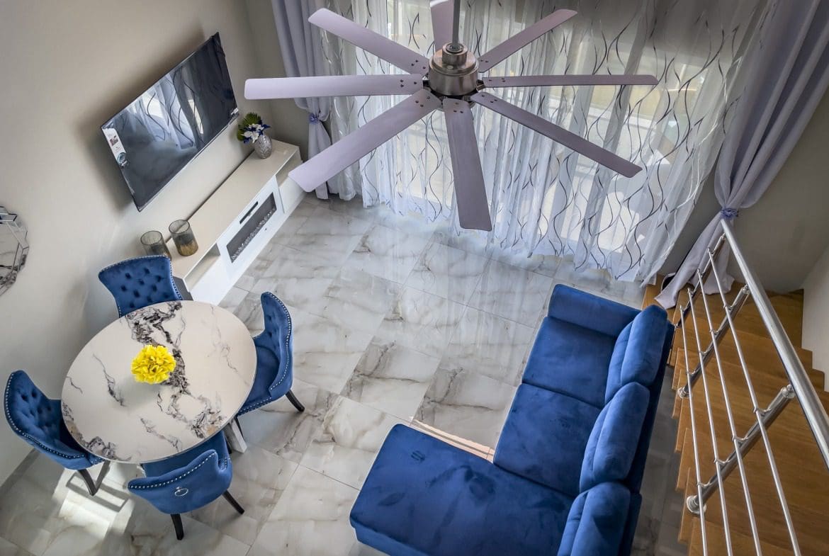 buyDRproperty Modern 1-Bedroom Condo living room with blue velvet sofa, dining table, and ceiling fan. Sosua Real Estate