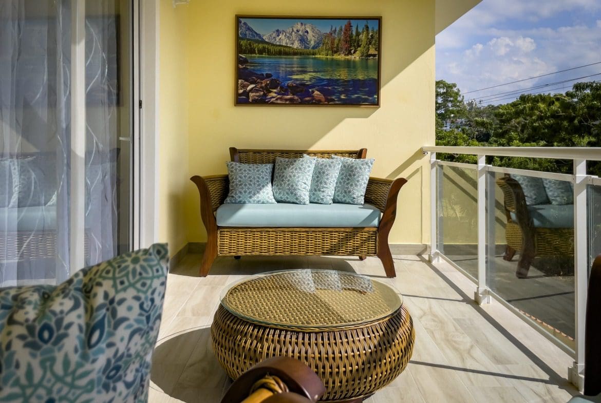 buyDRproperty Cozy outdoor seating area on a Modern 1-Bedroom Condo balcony with wicker furniture and mountain landscape artwork. Sosua Real Estate