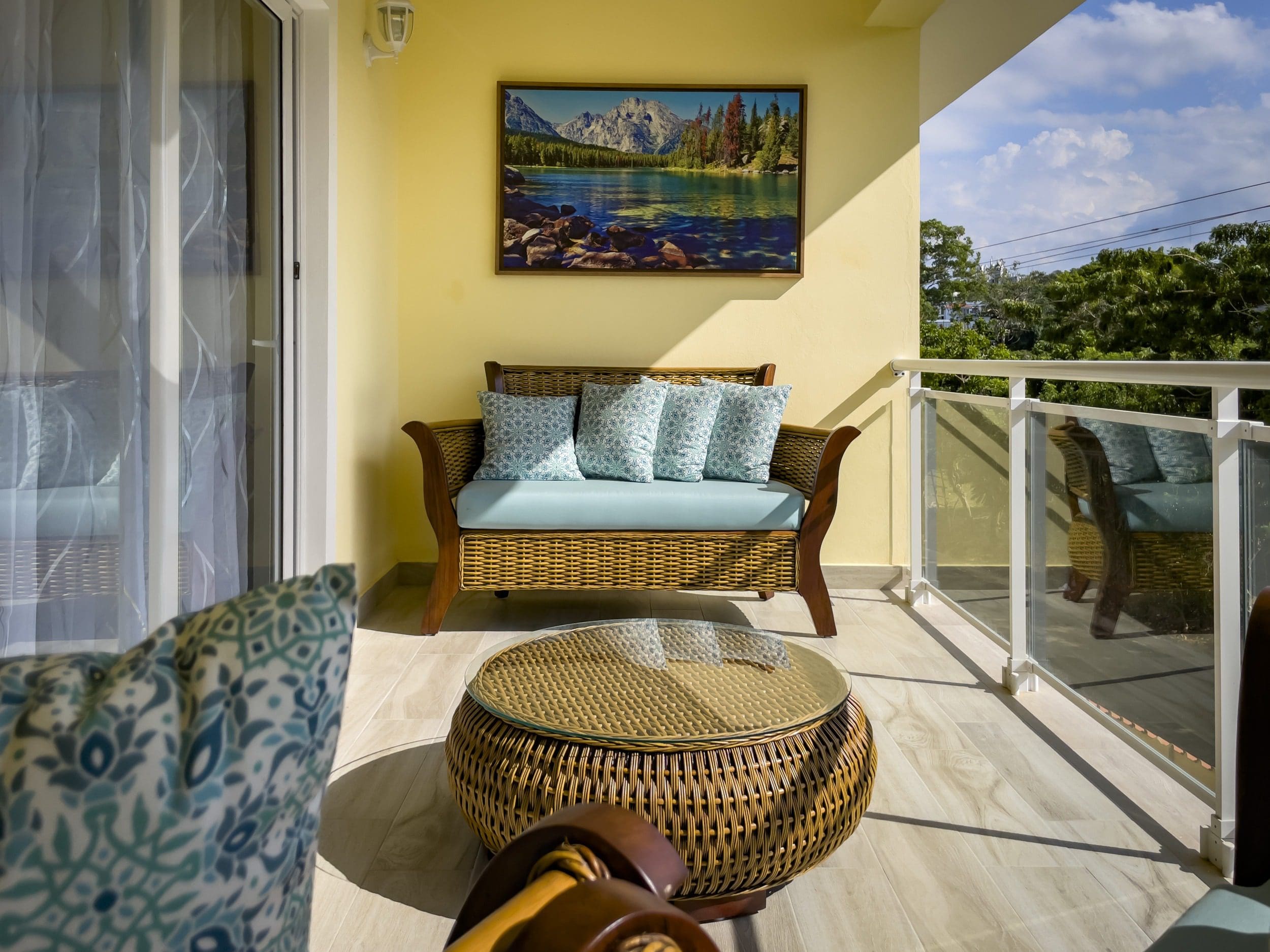 buyDRproperty Cozy outdoor seating area on a Modern 1-Bedroom Condo balcony with wicker furniture and mountain landscape artwork. Sosua Real Estate