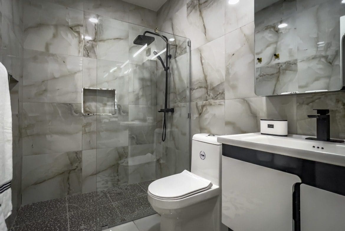 buyDRproperty Modern bathroom with marble tile, glass shower, and black fixtures in a 1-bedroom condo Sosua Real Estate