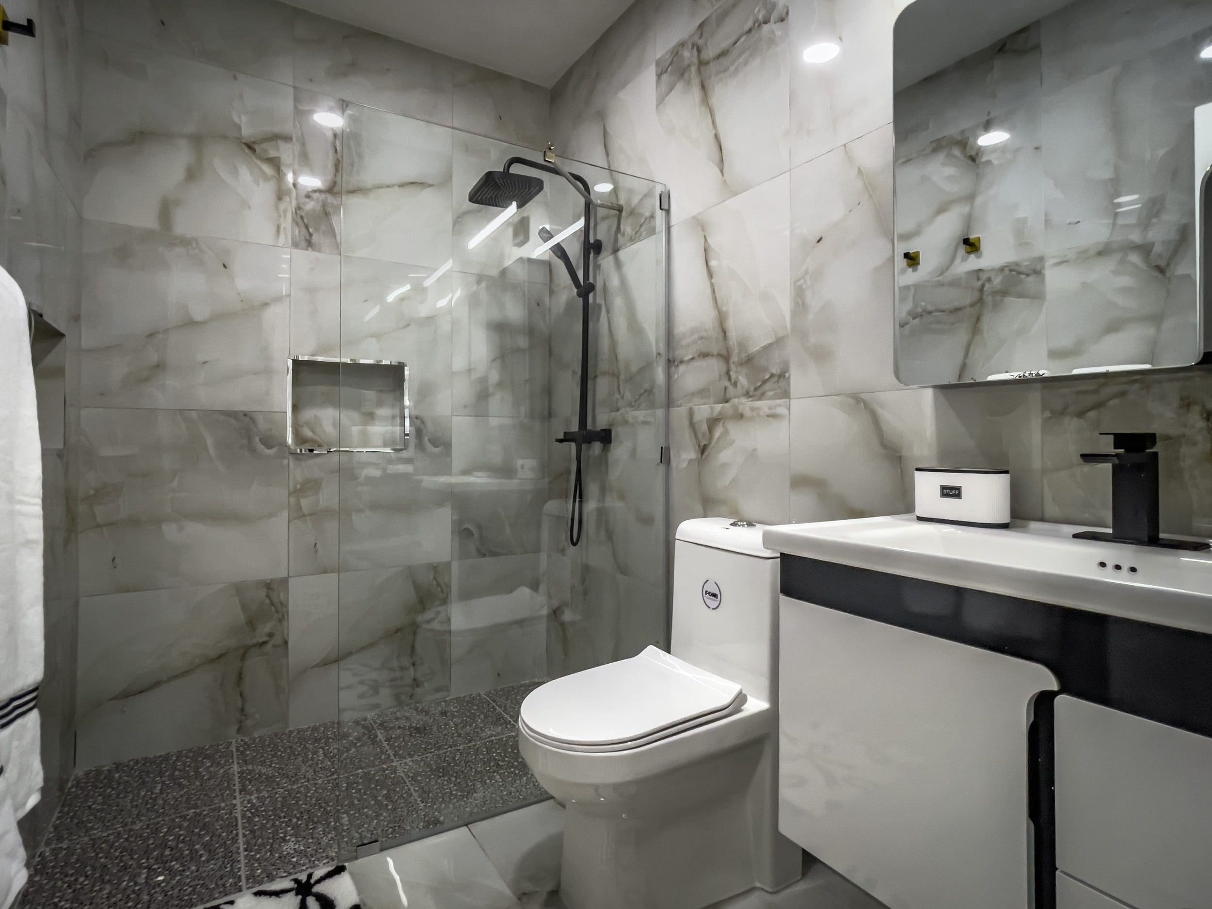 buyDRproperty Modern bathroom with marble tile, glass shower, and black fixtures in a 1-bedroom condo Sosua Real Estate