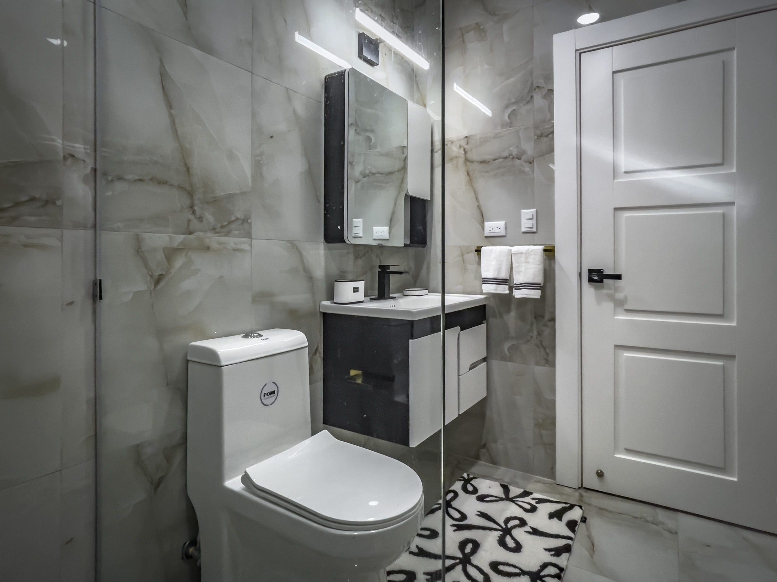 buyDRproperty Modern bathroom with white toilet, floating vanity, and marble tile. Sosua Real Estate