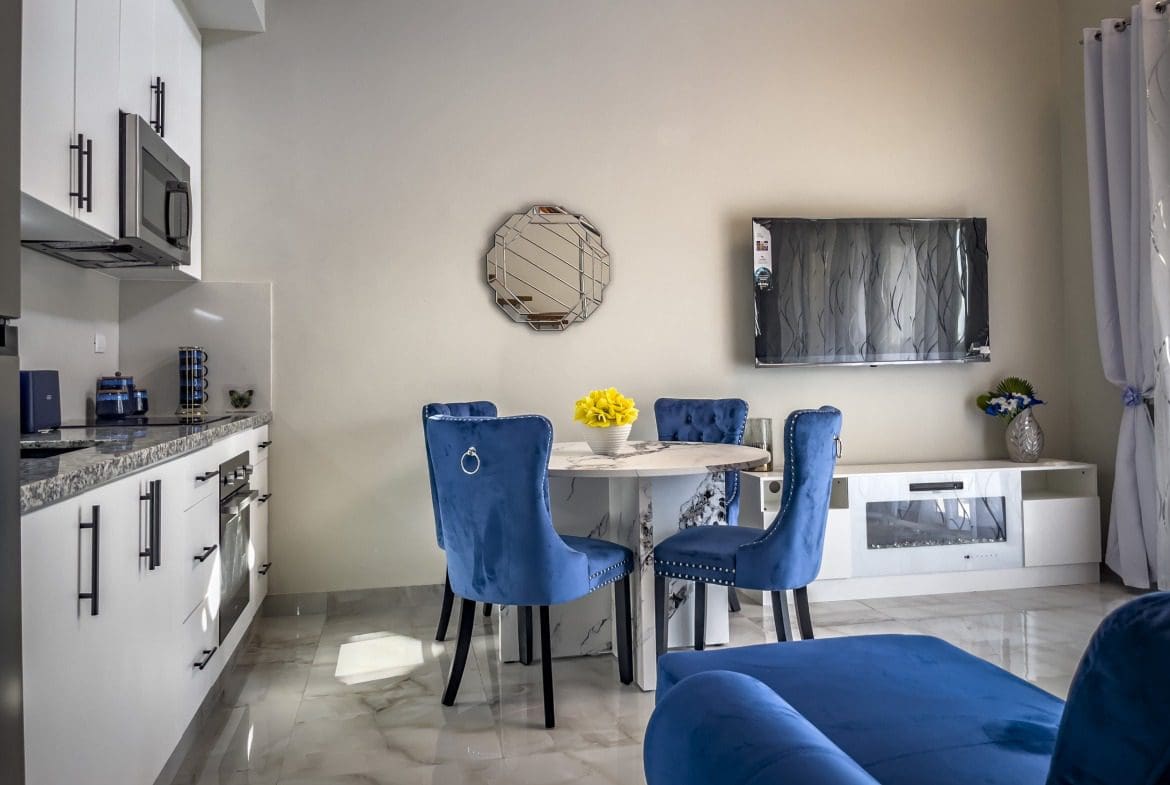 buyDRproperty Modern 1-bedroom condo living room with blue velvet chairs, marble table, and TV. Sosua Real Estate