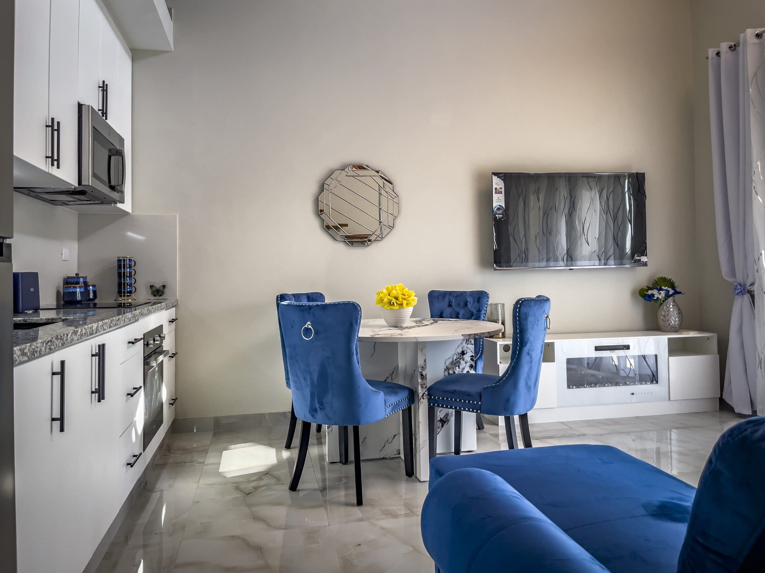 buyDRproperty Modern 1-bedroom condo living room with blue velvet chairs, marble table, and TV. Sosua Real Estate
