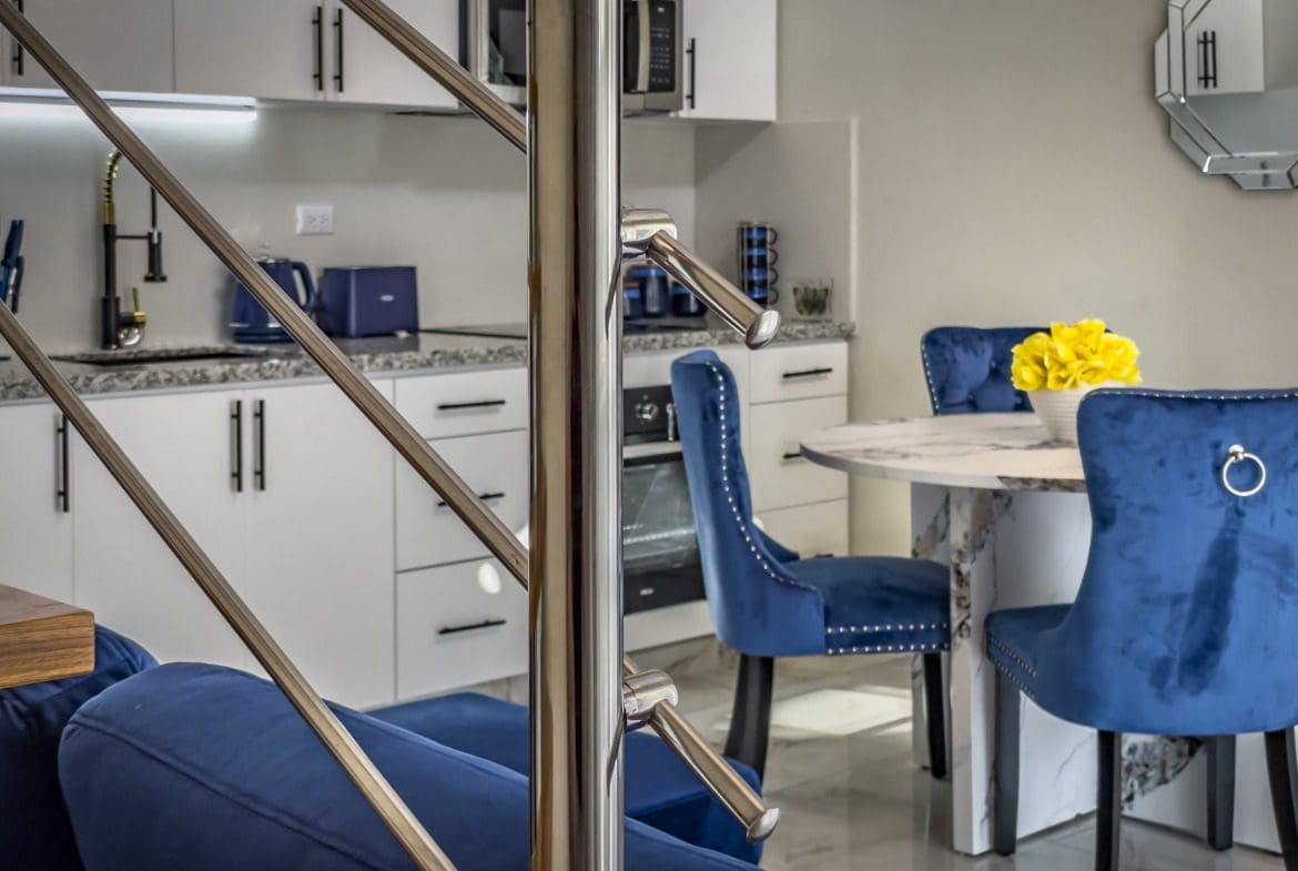 buyDRproperty Modern 1-Bedroom Condo interior with stainless steel staircase and blue velvet dining chairs. Sosua Real Estate