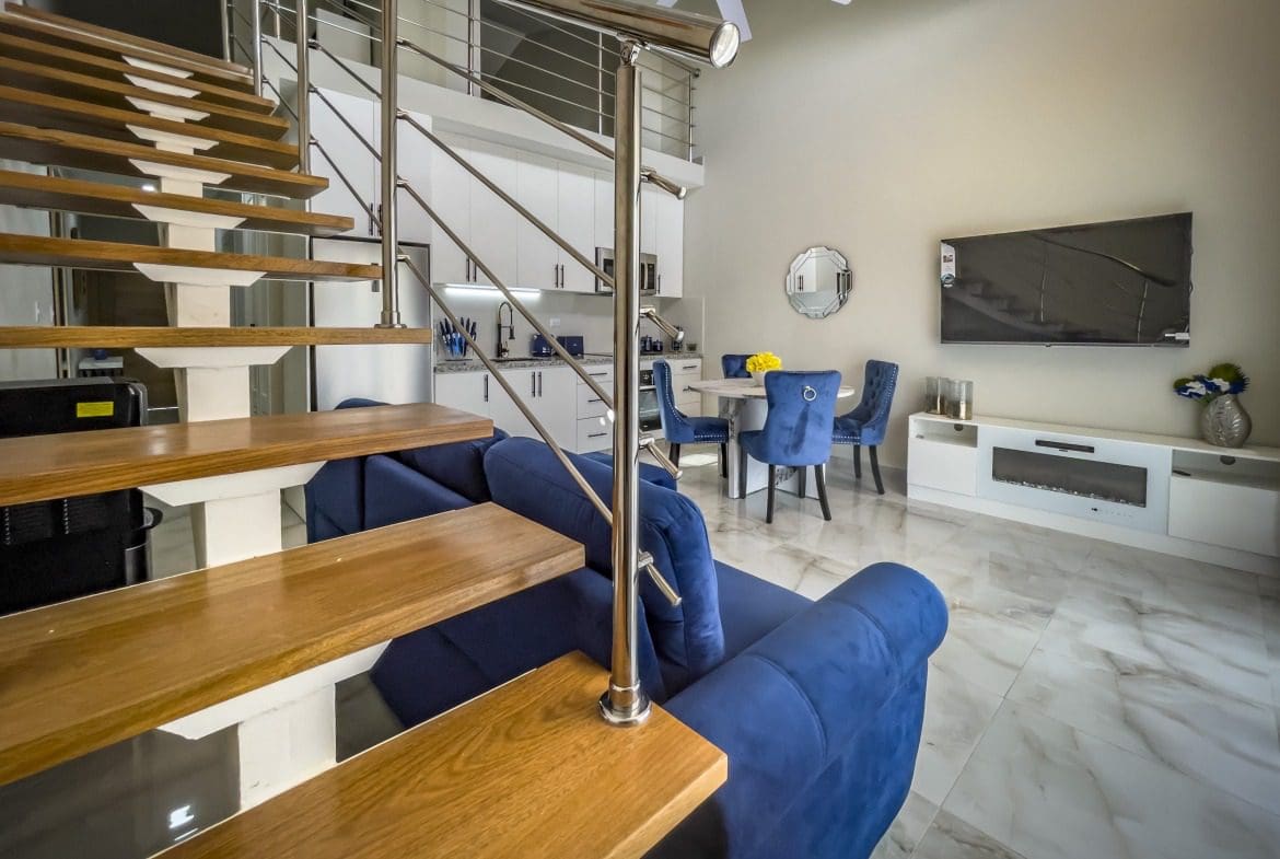 buyDRproperty Modern 1-Bedroom Condo living room with blue sofa, stairs, and dining area Sosua Real Estate