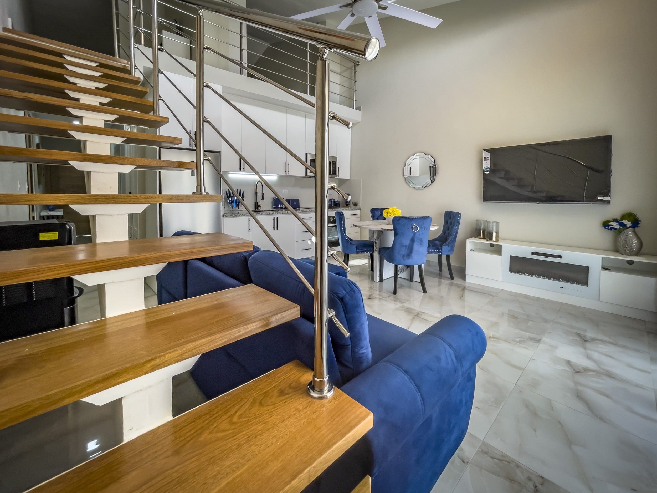 buyDRproperty Modern 1-Bedroom Condo living room with blue sofa, stairs, and dining area Sosua Real Estate