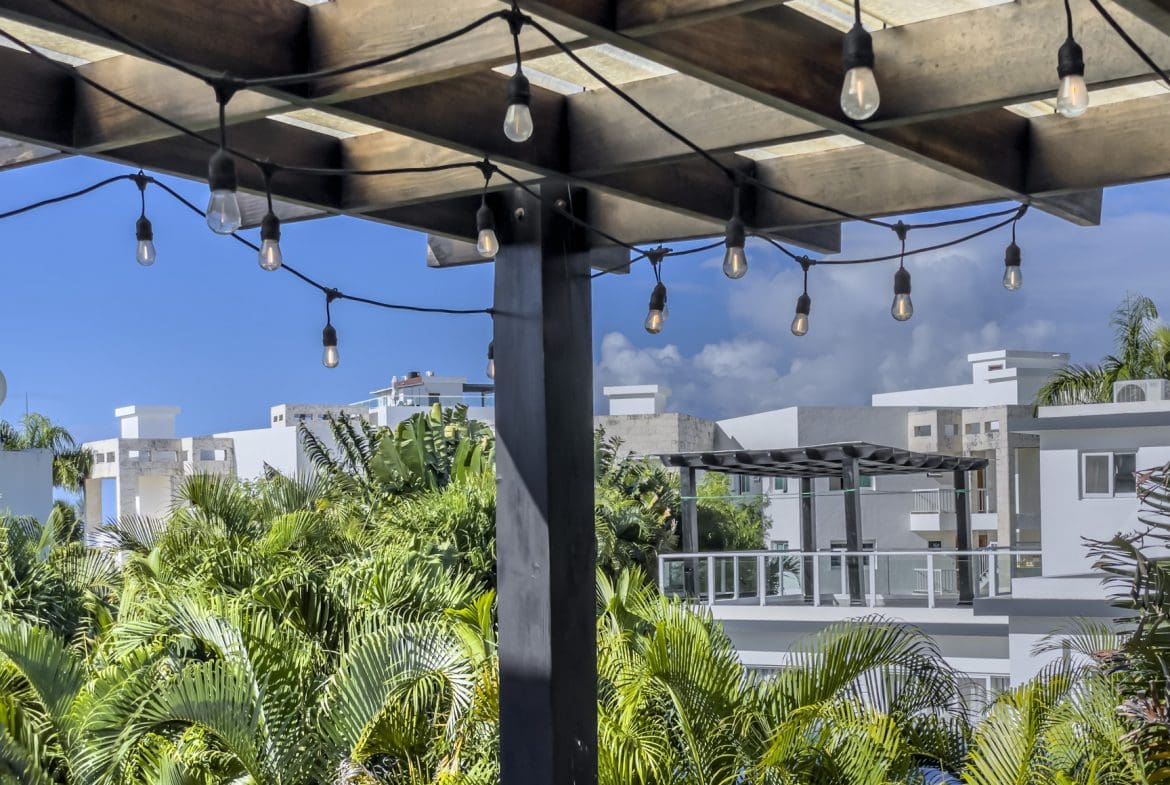 buyDRproperty String lights under a wooden pergola, overlooking lush tropical foliage and modern villas in Sosúa Ocean Village, Dominican Republic. Sosua Real Estate
