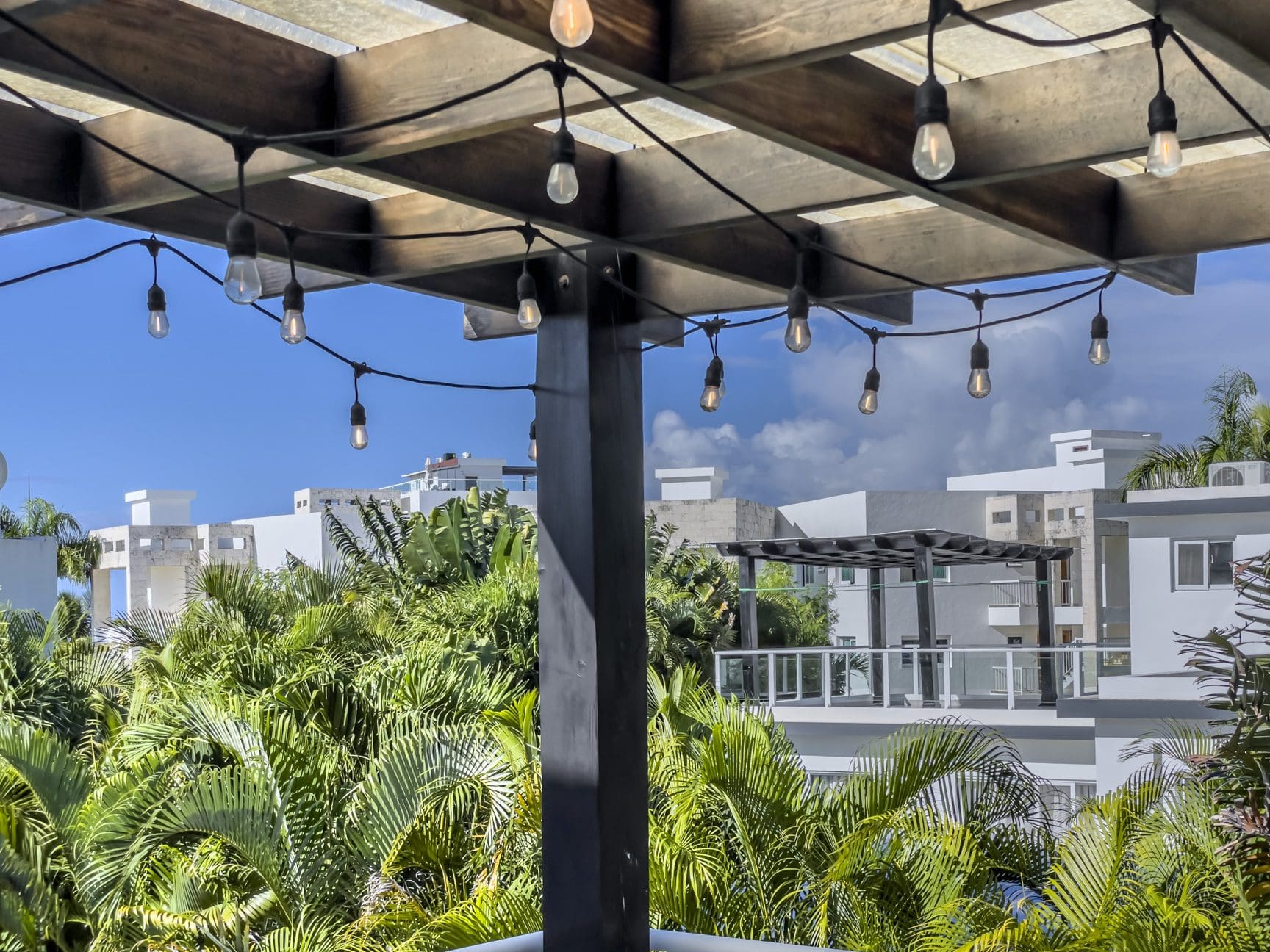 buyDRproperty String lights under a wooden pergola, overlooking lush tropical foliage and modern villas in Sosúa Ocean Village, Dominican Republic. Sosua Real Estate