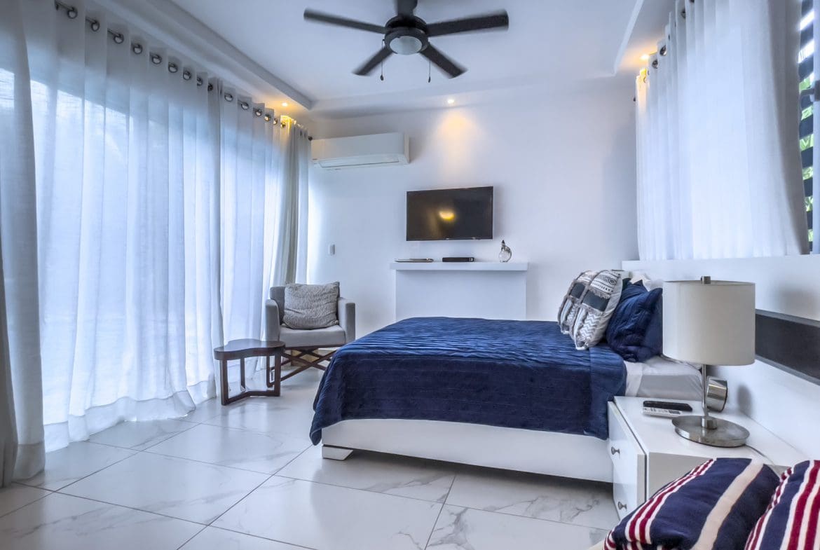 buyDRproperty Modern 3-bedroom villa bedroom in Sosúa Ocean Village with ocean view. Luxurious design with white walls and blue bedding. Sosua Real Estate