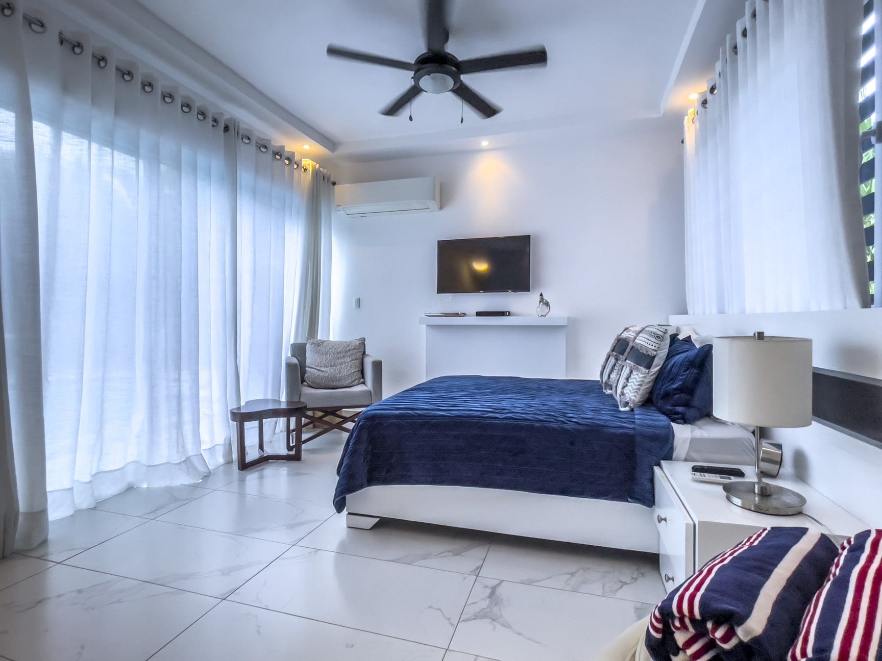 buyDRproperty Modern 3-bedroom villa bedroom in Sosúa Ocean Village with ocean view. Luxurious design with white walls and blue bedding. Sosua Real Estate