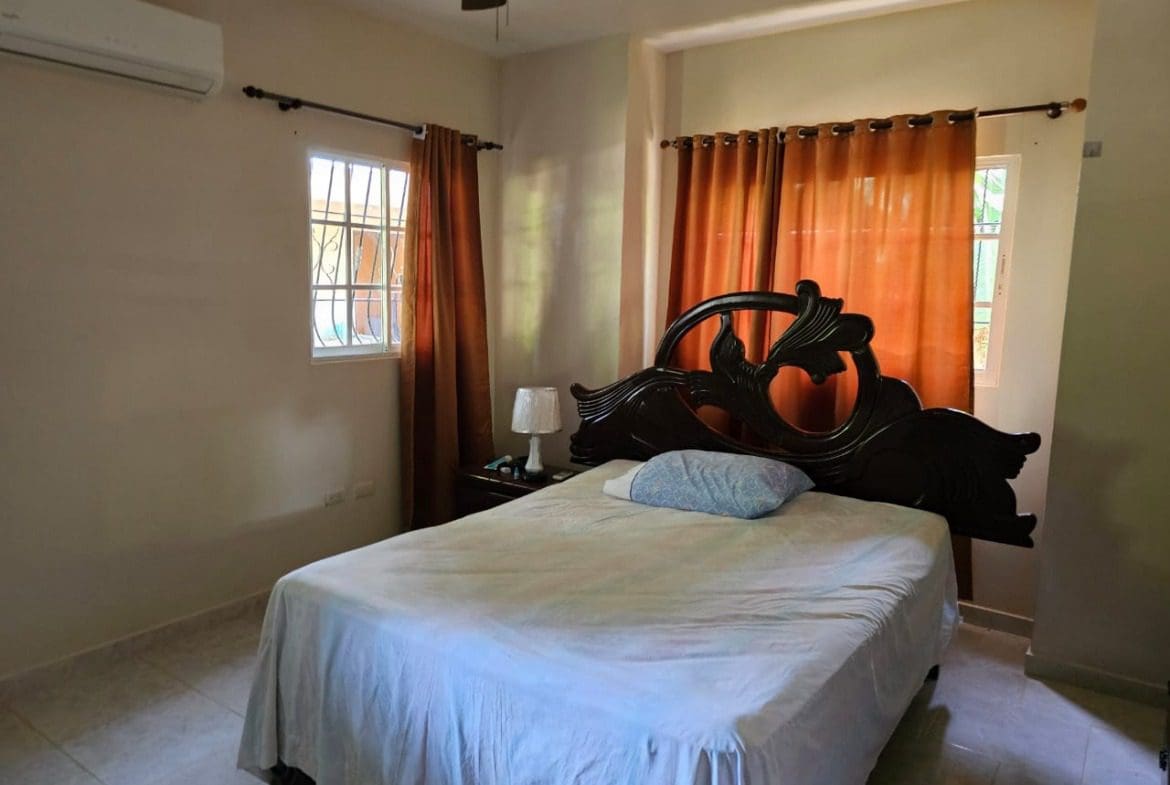 buyDRproperty Bedroom in Cabarete house for sale with ornate wooden headboard and orange curtains. Sosua Real Estate