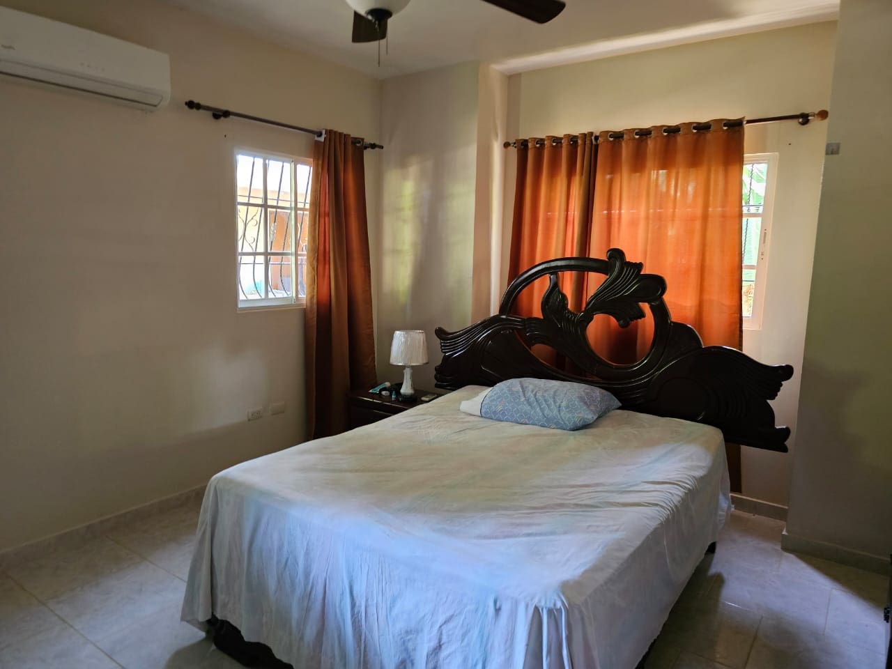 buyDRproperty Bedroom in Cabarete house for sale with ornate wooden headboard and orange curtains. Sosua Real Estate