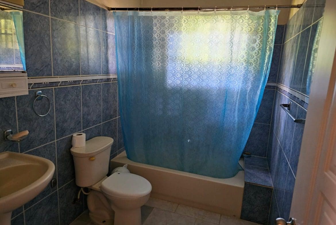 buyDRproperty Bathroom with blue tiles, toilet, sink, and shower curtain. Sosua Real Estate