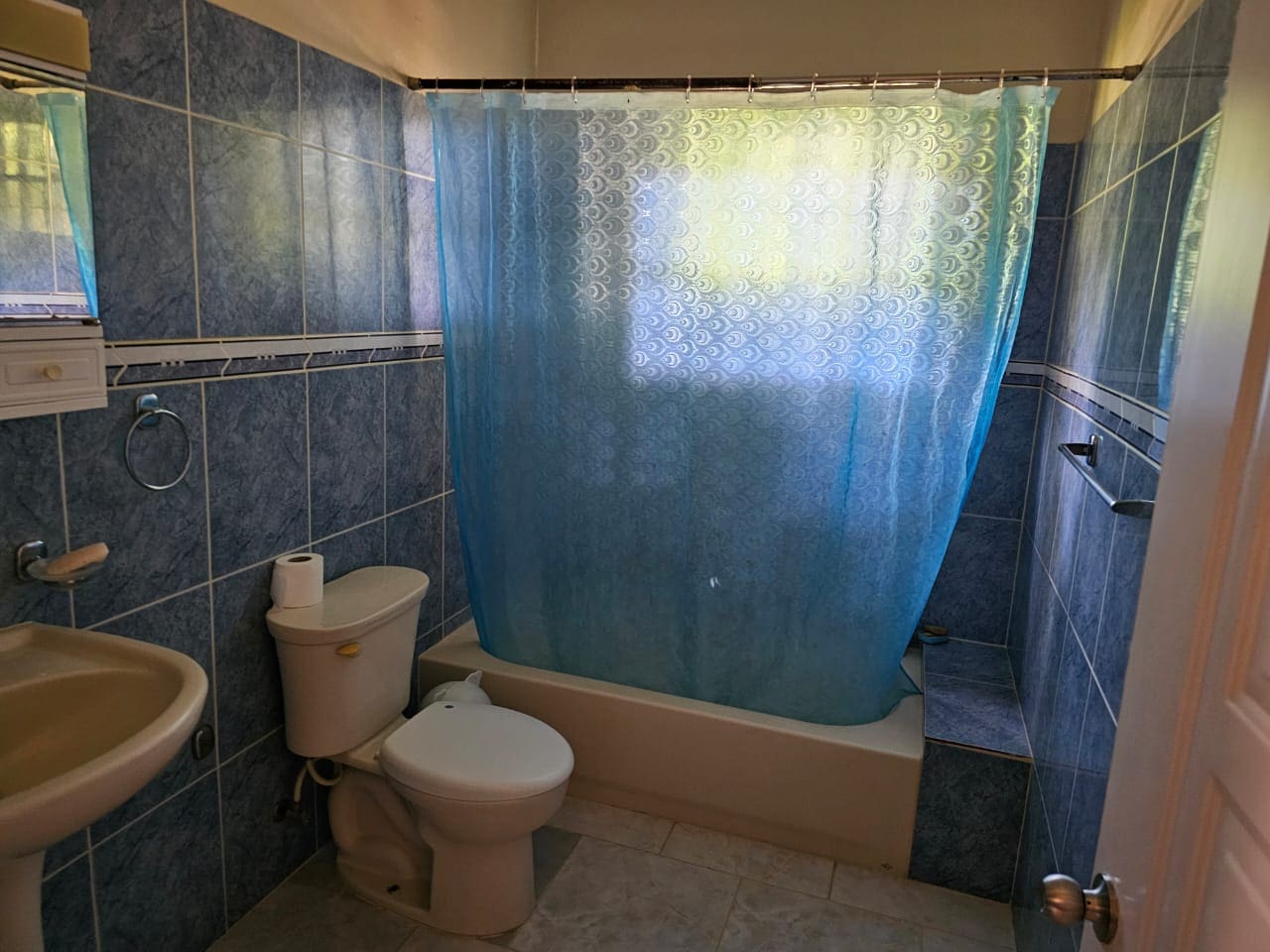 buyDRproperty Bathroom with blue tiles, toilet, sink, and shower curtain. Sosua Real Estate