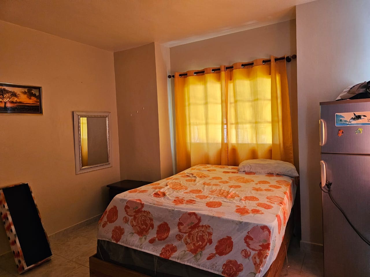 buyDRproperty Bedroom with floral bedspread, yellow curtains, and refrigerator. Sosua Real Estate