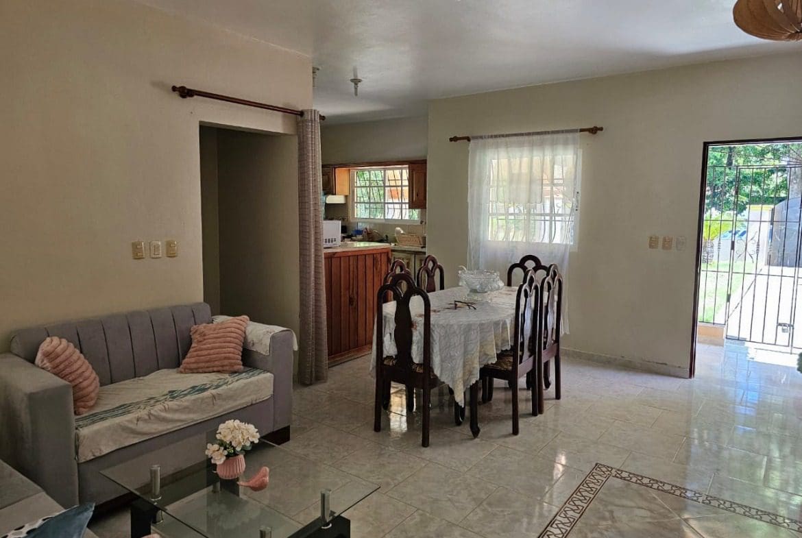 buyDRproperty Living and dining area with gray sofa, dining table, and open doorway in a house for sale. Sosua Real Estate
